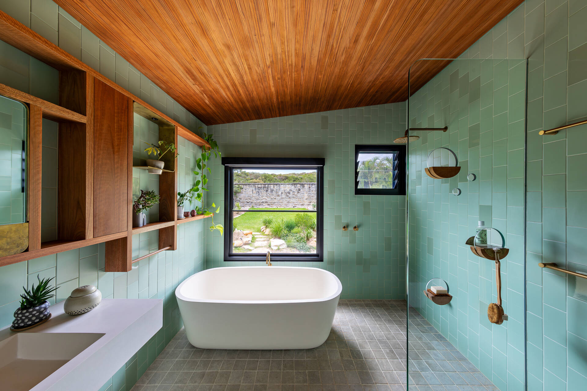 A modern bathroom lined with green-blue and grey tiles, and warm wood accents.