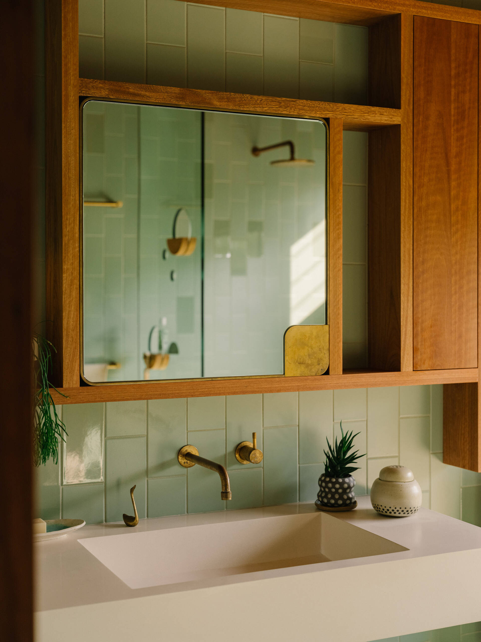 A modern bathroom lined with green-blue and grey tiles, and warm wood accents.