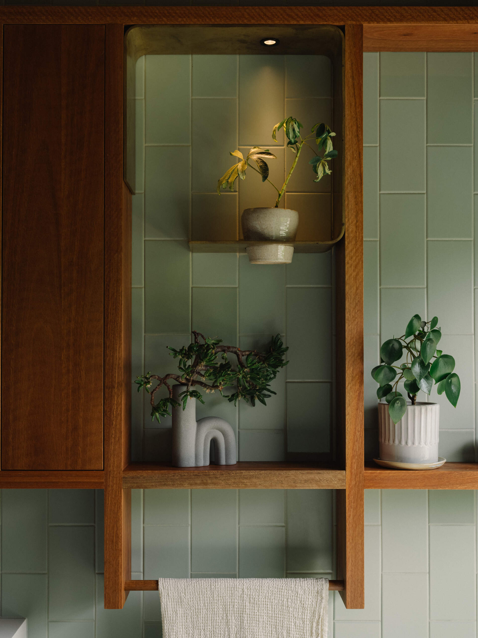 A modern bathroom lined with green-blue and grey tiles, and warm wood accents.