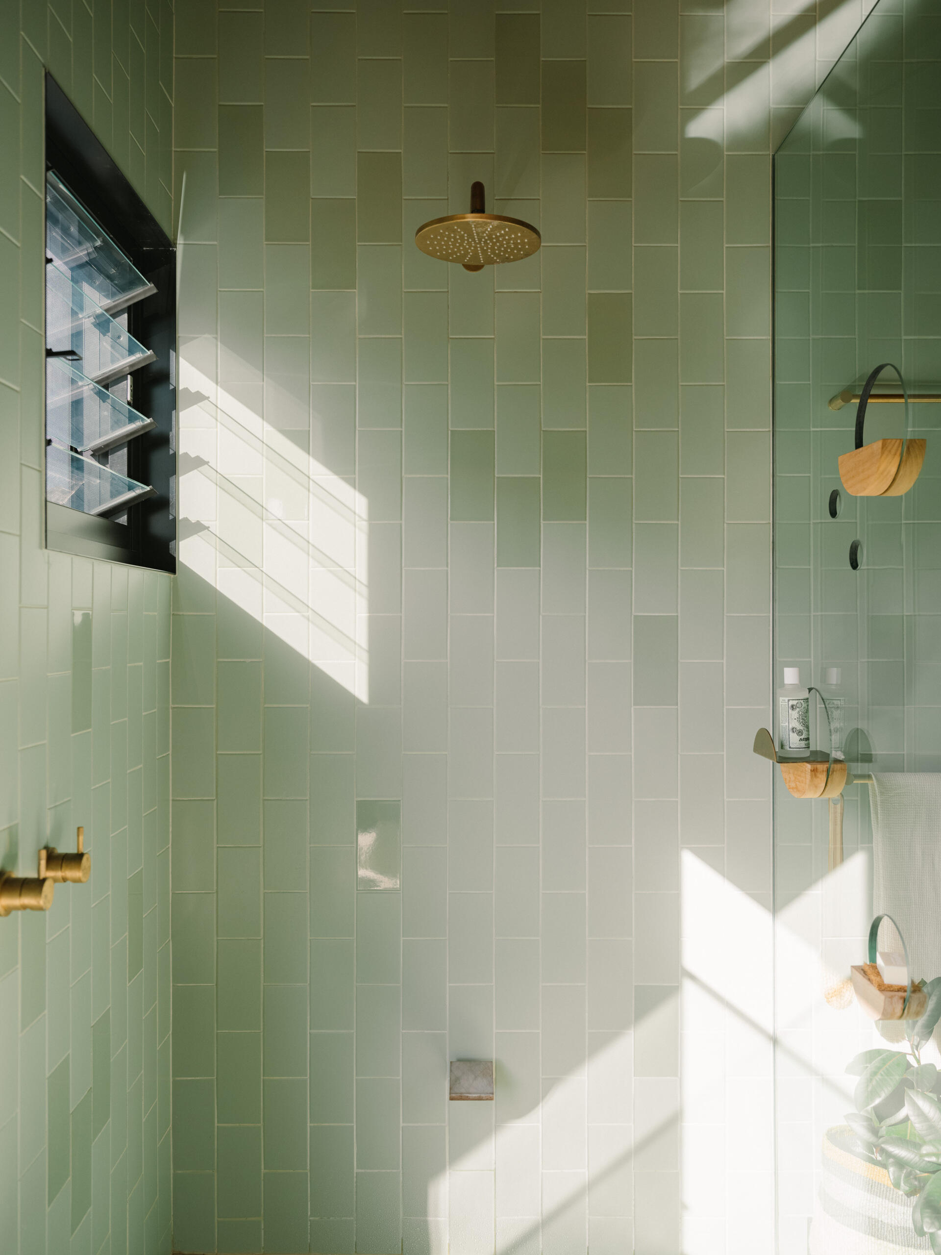 A modern bathroom lined with green-blue and grey tiles, and warm wood accents.