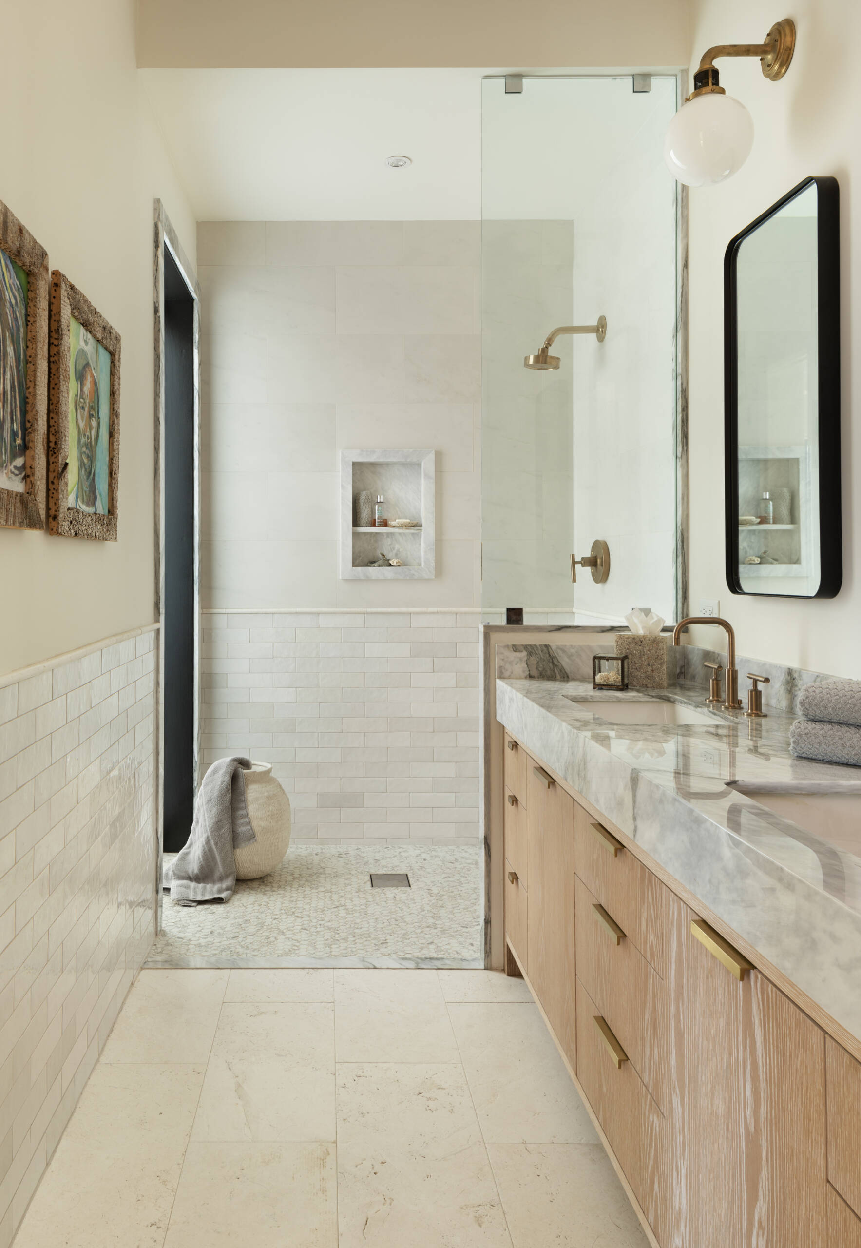 Serene bathroom finished in light stone, white tile, warm wood vanities, and brushed brass fixtures, creating a spa-like atmosphere grounded in simplicity.