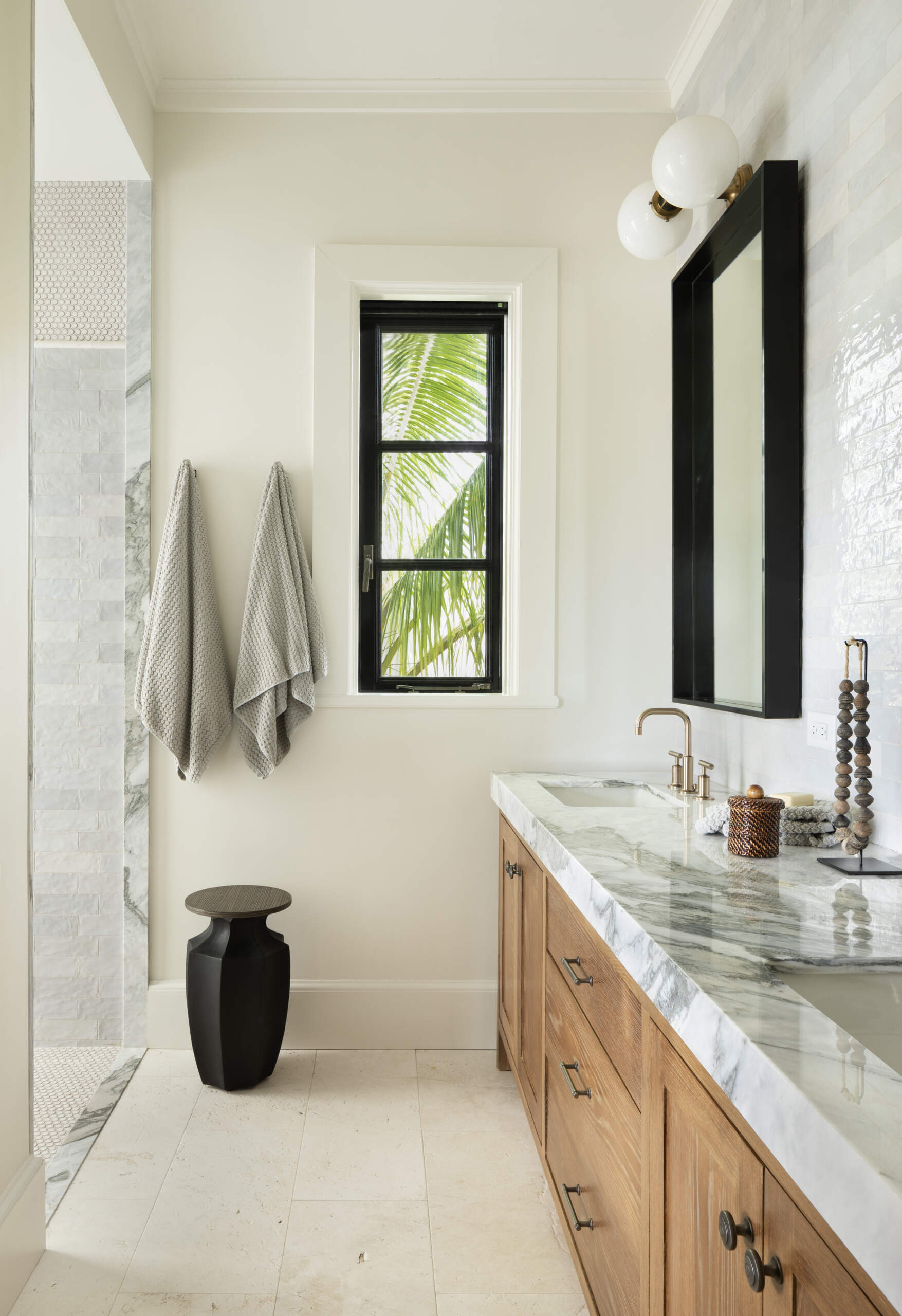 Serene bathroom finished in light stone, white tile, warm wood vanities, and brushed brass fixtures, creating a spa-like atmosphere grounded in simplicity.