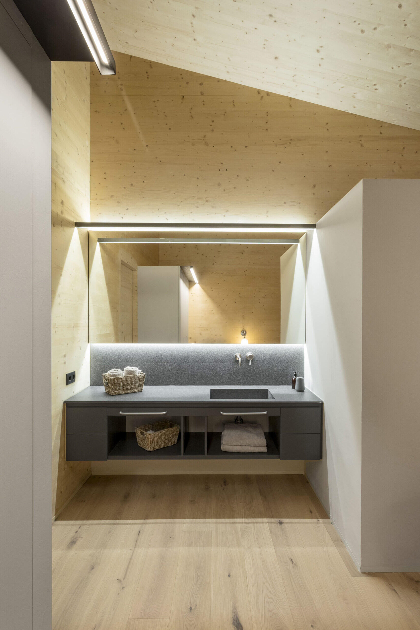 Grey cabinetry, backlit mirrors, and minimalist lighting stand out against warm wood walls and ceilings.