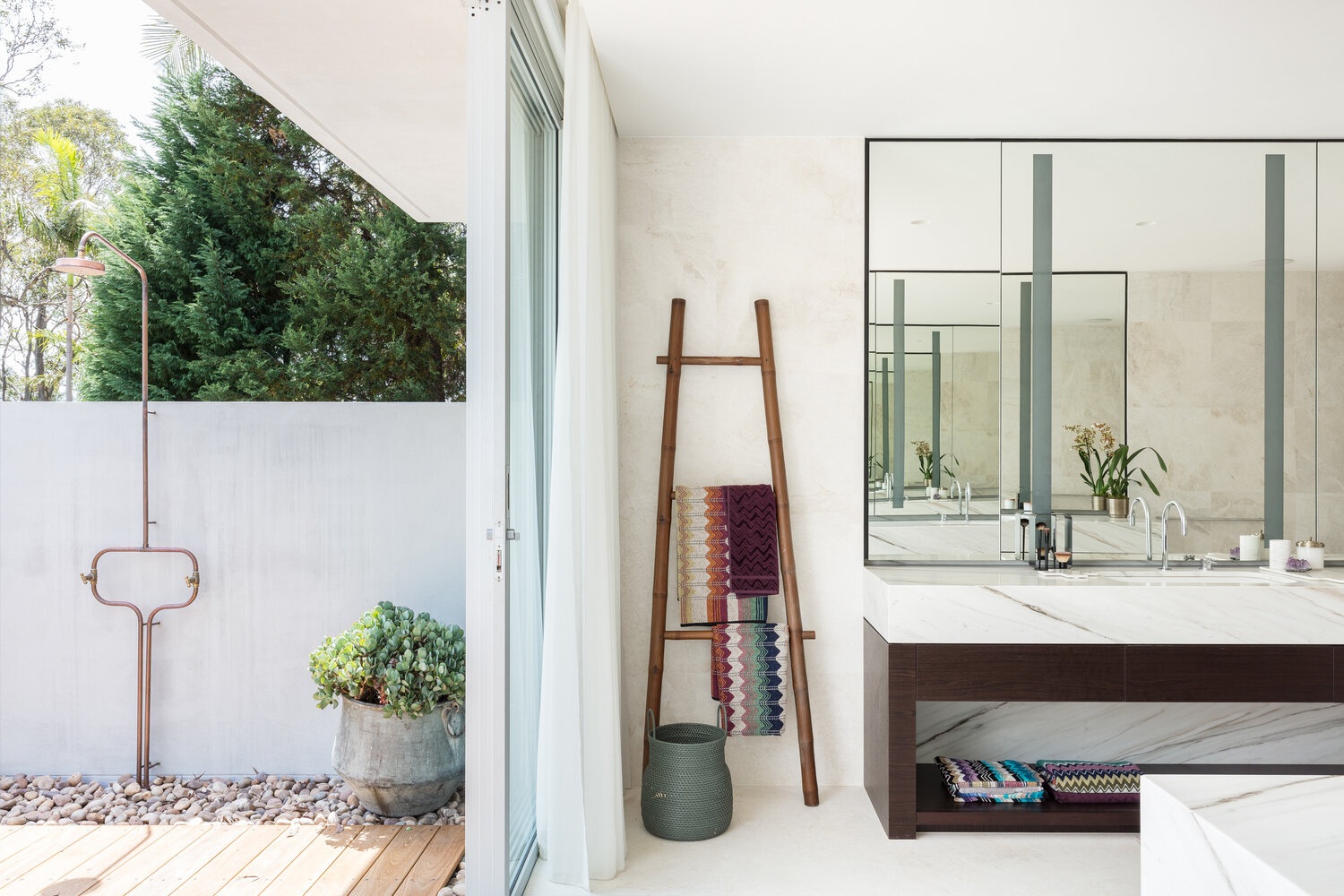 Sliding glass doors reveal an outdoor shower, blending indoor luxury with a natural, open air bathing experience.