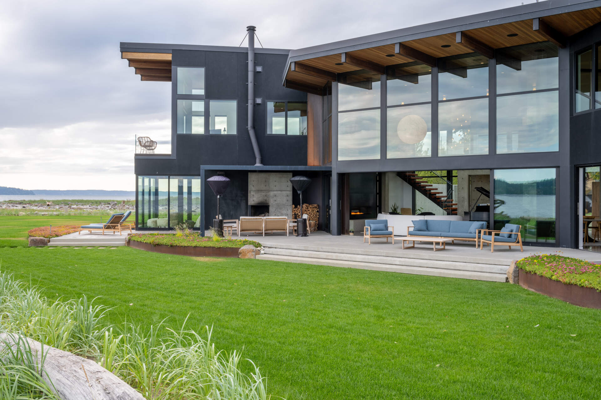 The terrace of this modern house runs along the water facing side of the home and connects to an lounge with a fireplace as well as an outdoor cooking patio supports with dining area. These exterior spaces are oriented to fully engage with the peninsula setting and surrounding water.