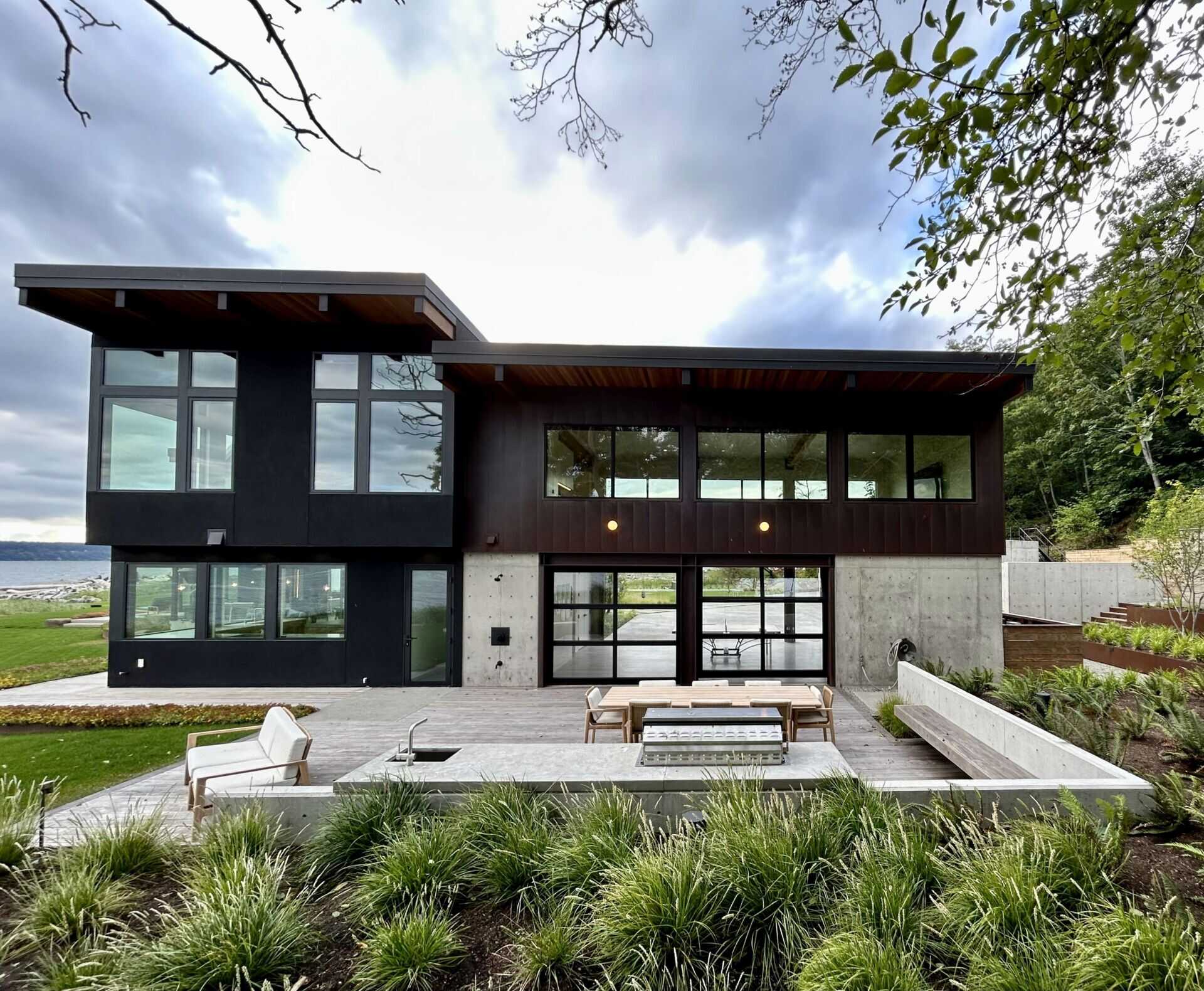 The terrace of this modern house runs along the water facing side of the home and connects to an lounge with a fireplace as well as an outdoor cooking patio supports with dining area. These exterior spaces are oriented to fully engage with the peninsula setting and surrounding water.
