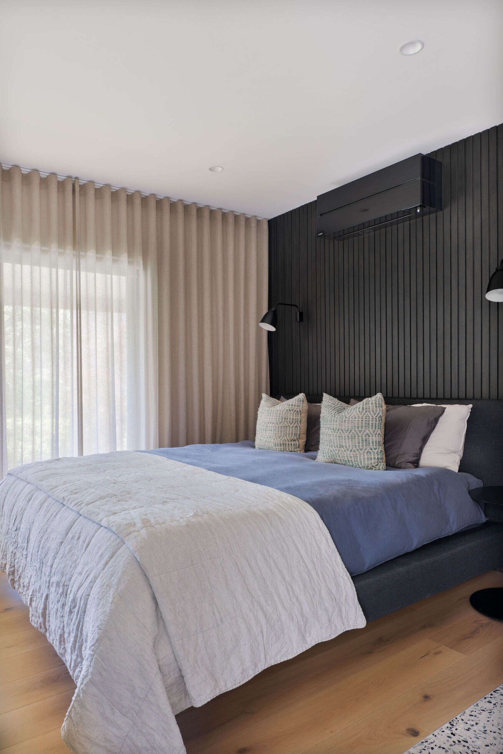 This primary bedroom mirrors the hotel like quality the homeowners dreamed of. A king bed sits against the same Ravenswood black wall panel seen throughout the home, giving the room visual continuity. Soft window treatments, a dedicated study nook and three walls of robes create a generous and refined retreat.