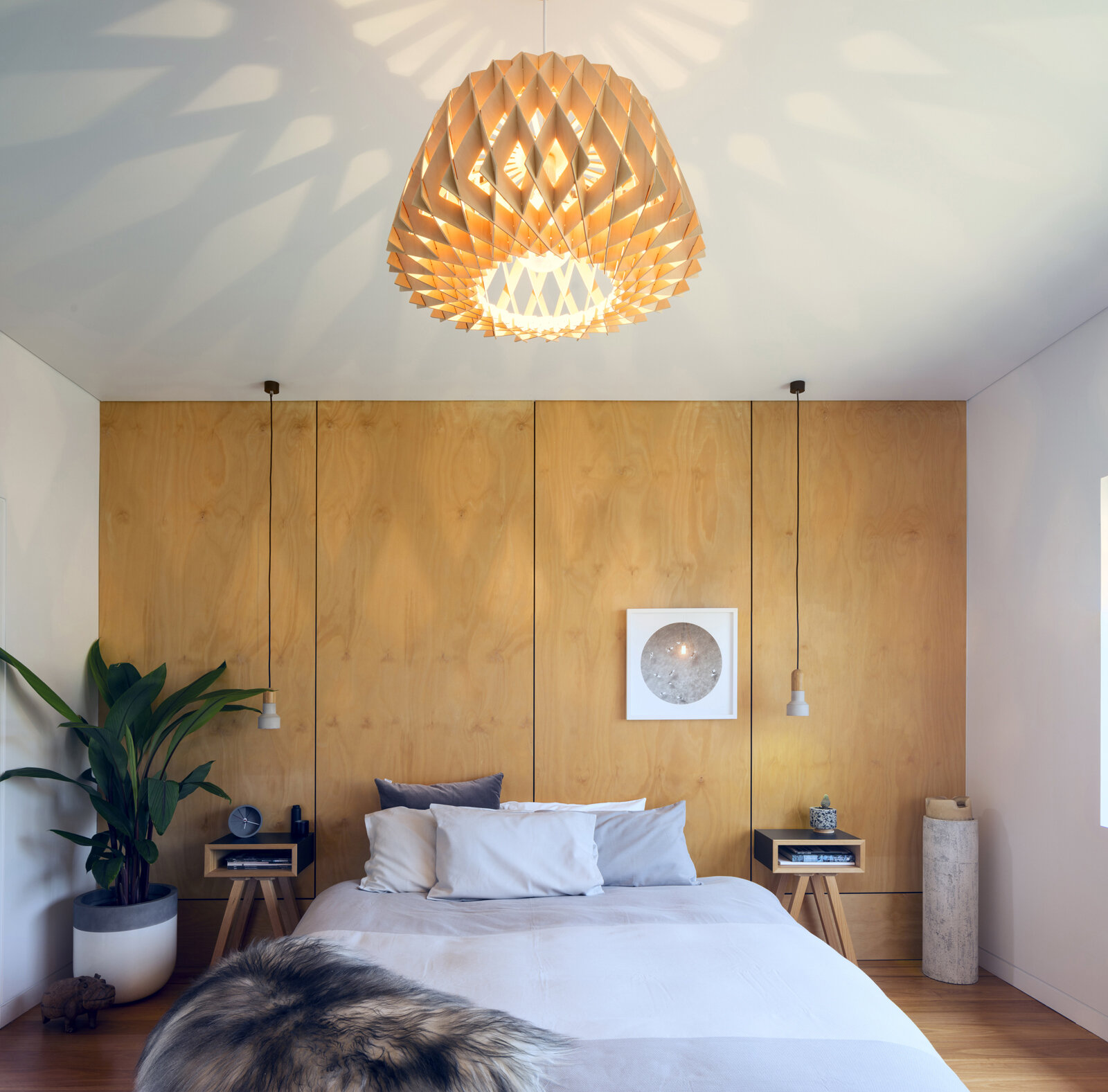 A minimalist primary bedroom uses a full timber wall as both headboard and architectural feature.