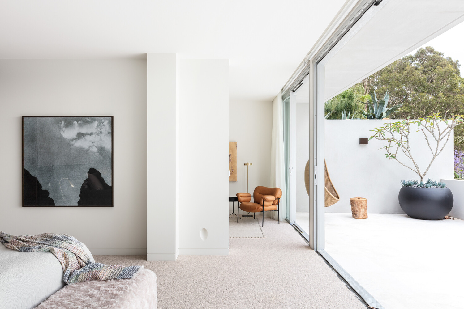 This primary bedroom opens onto a balcony with a hanging chair and planter, offering a serene retreat with views of the water.