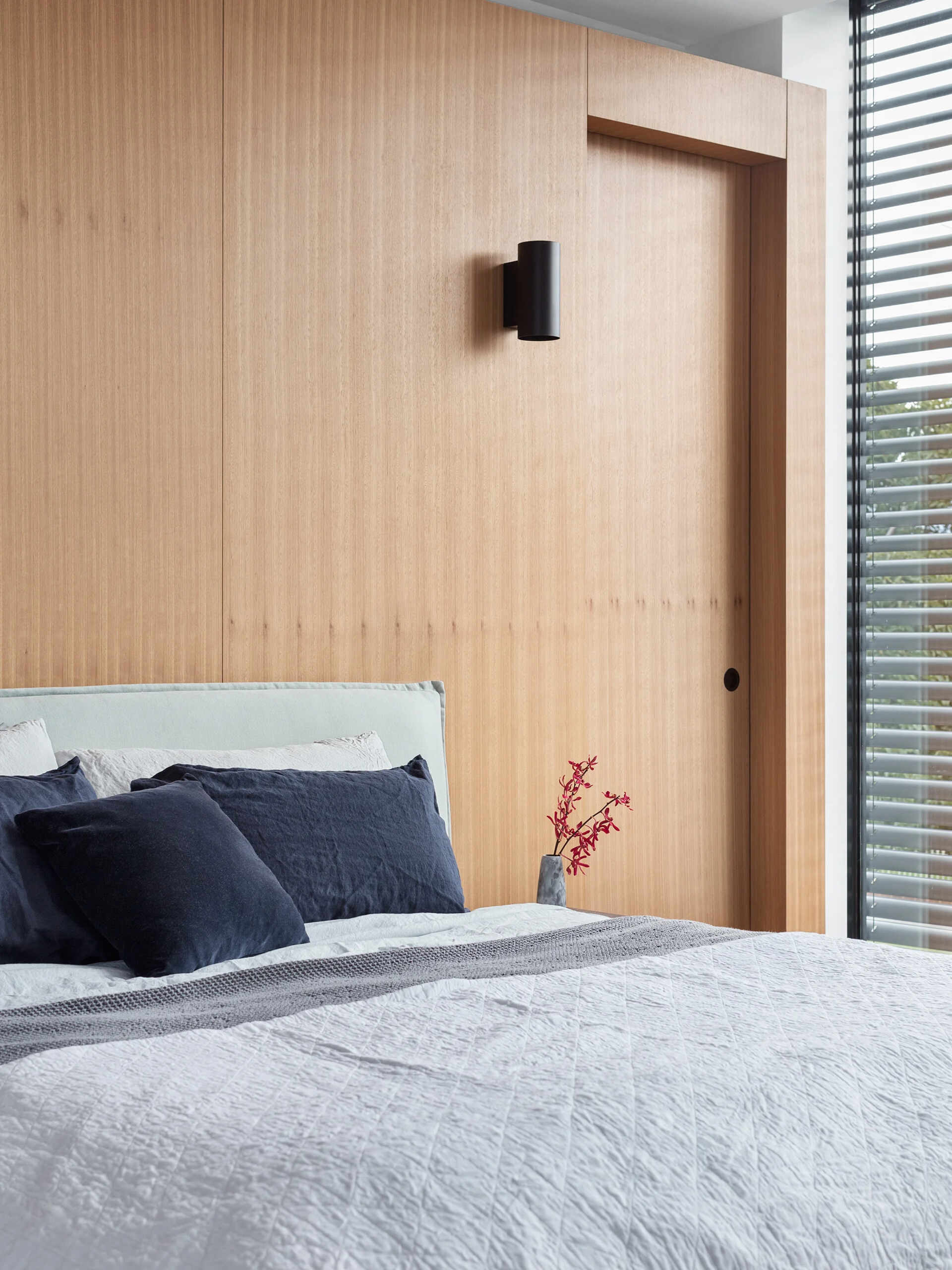 A modern bedroom with a warm wood accent wall and built-in closets combines style and comfort.