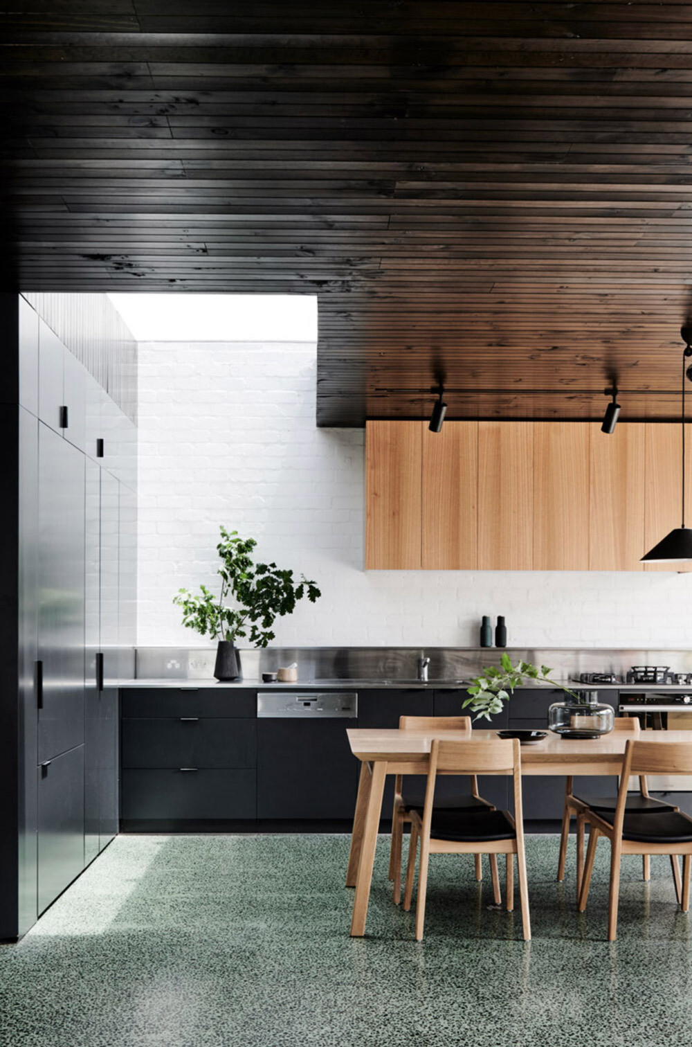 A sleek dark kitchen hides appliances behind cabinetry and reflects light with a polished stainless steel backsplash.