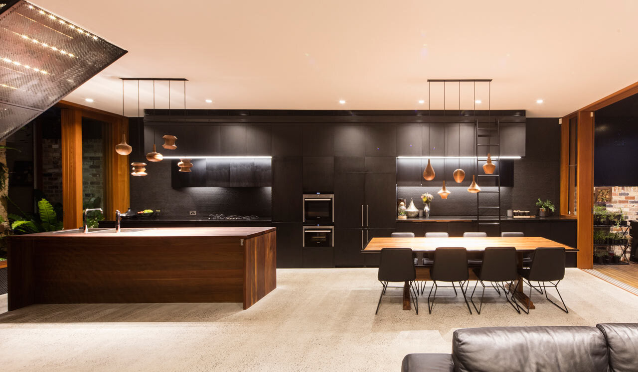 Sleek black cabinetry runs from kitchen to dining, balanced by warm timber and concrete floors for a striking modern look.