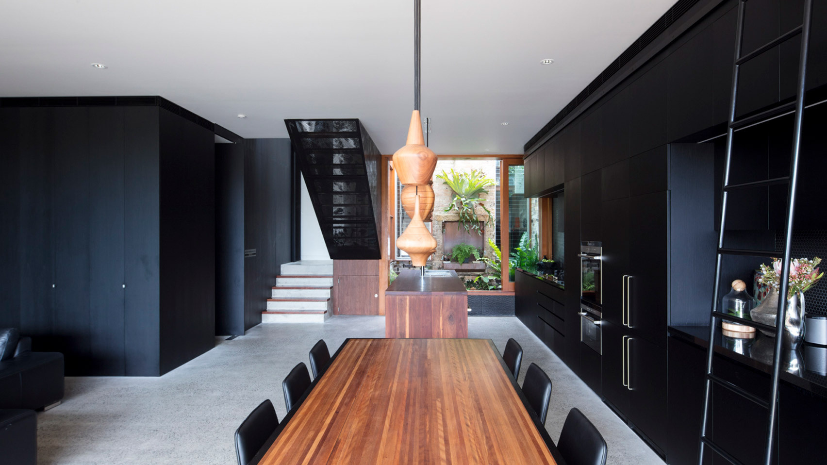 Sleek black cabinetry runs from kitchen to dining, balanced by warm timber and concrete floors for a striking modern look.