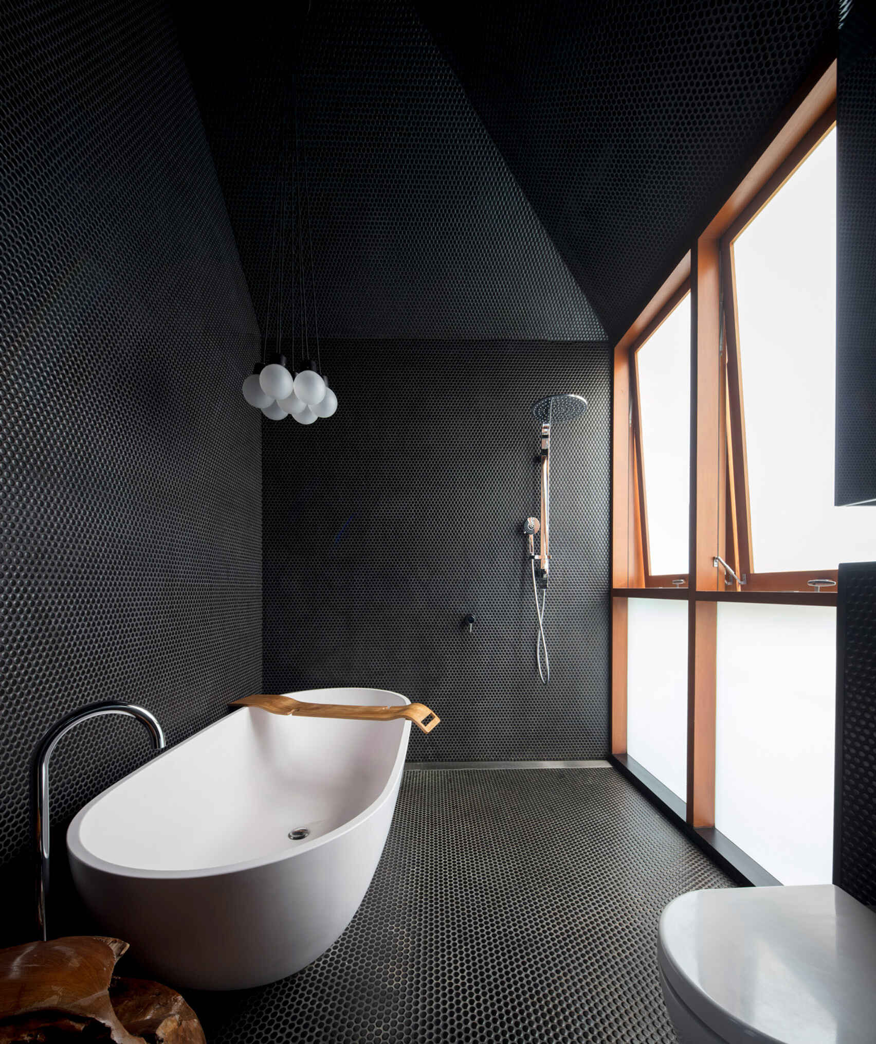 Black penny tiles and a frosted window create a moody yet bright bathroom beside the kitchen and stairs.