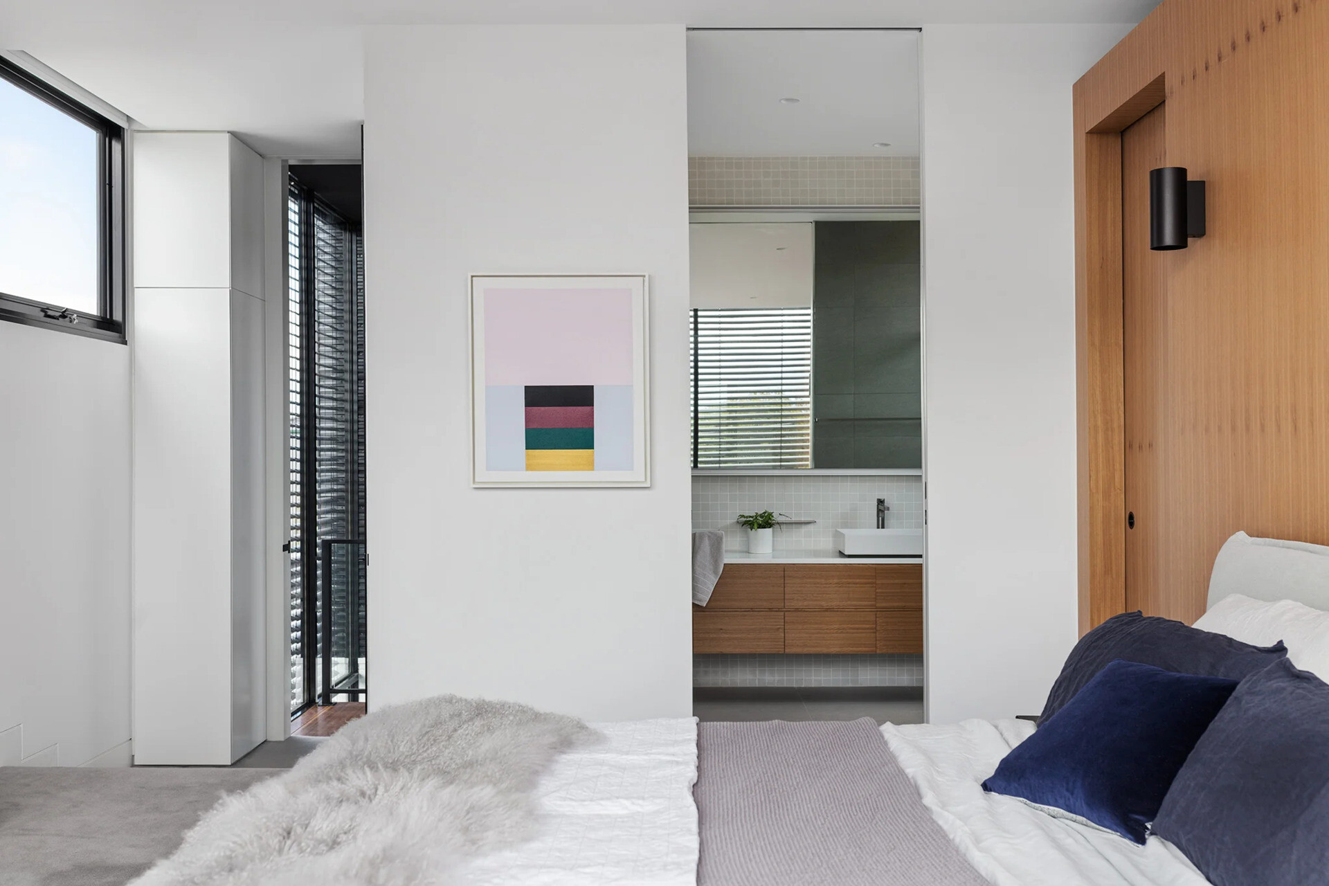 A light, modern ensuite with wood vanity, white basin, and subtle square tiles creates a serene retreat.