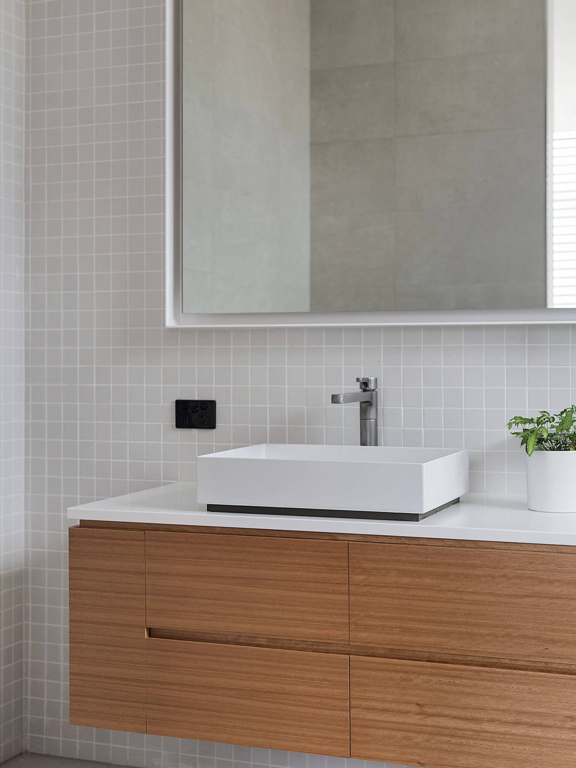 A light, modern ensuite with wood vanity, white basin, and subtle square tiles creates a serene retreat.