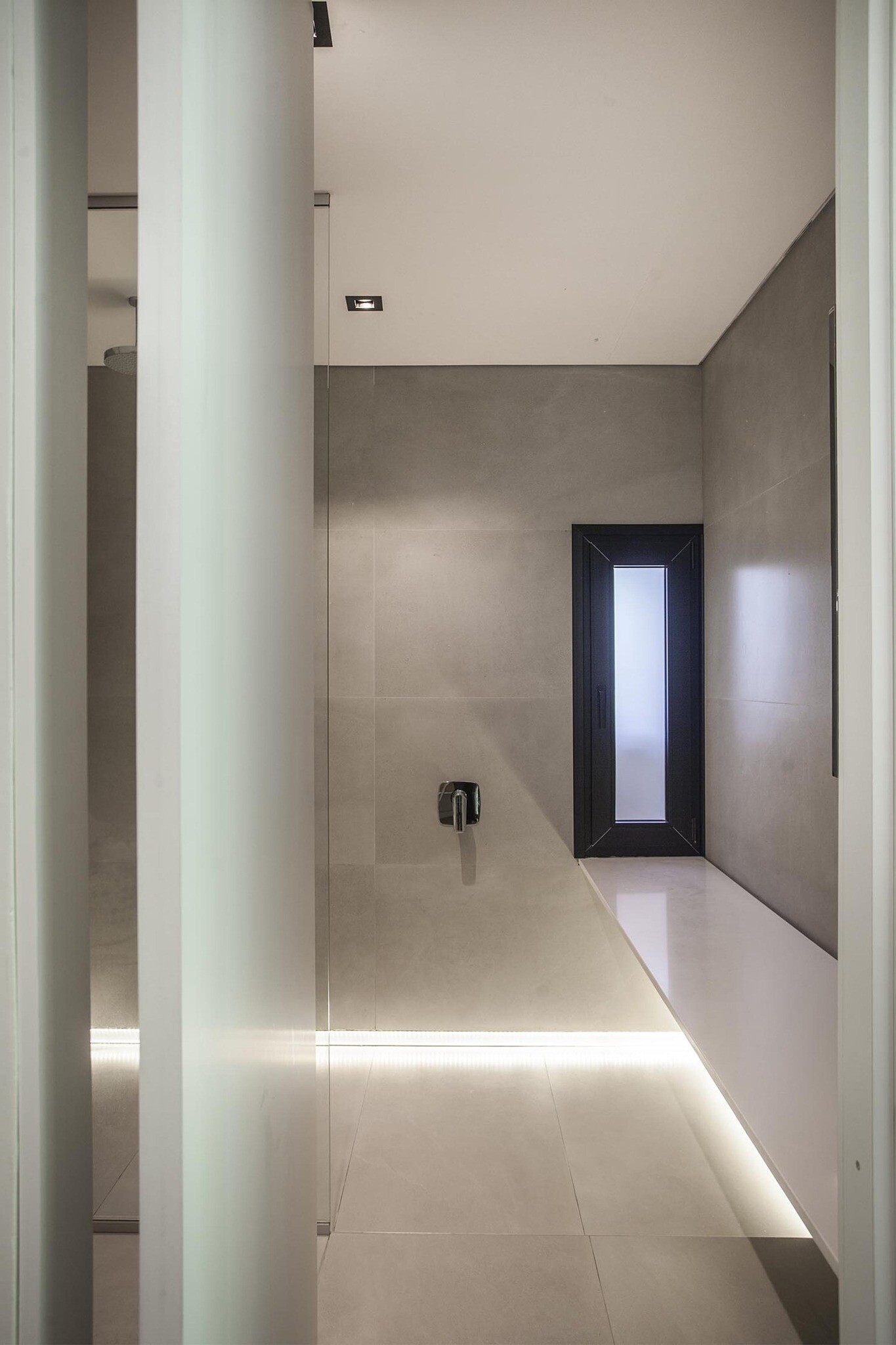 Grey tiled walls and subtle floor level lighting create a calm, architectural bathroom with a distinctive light feature.