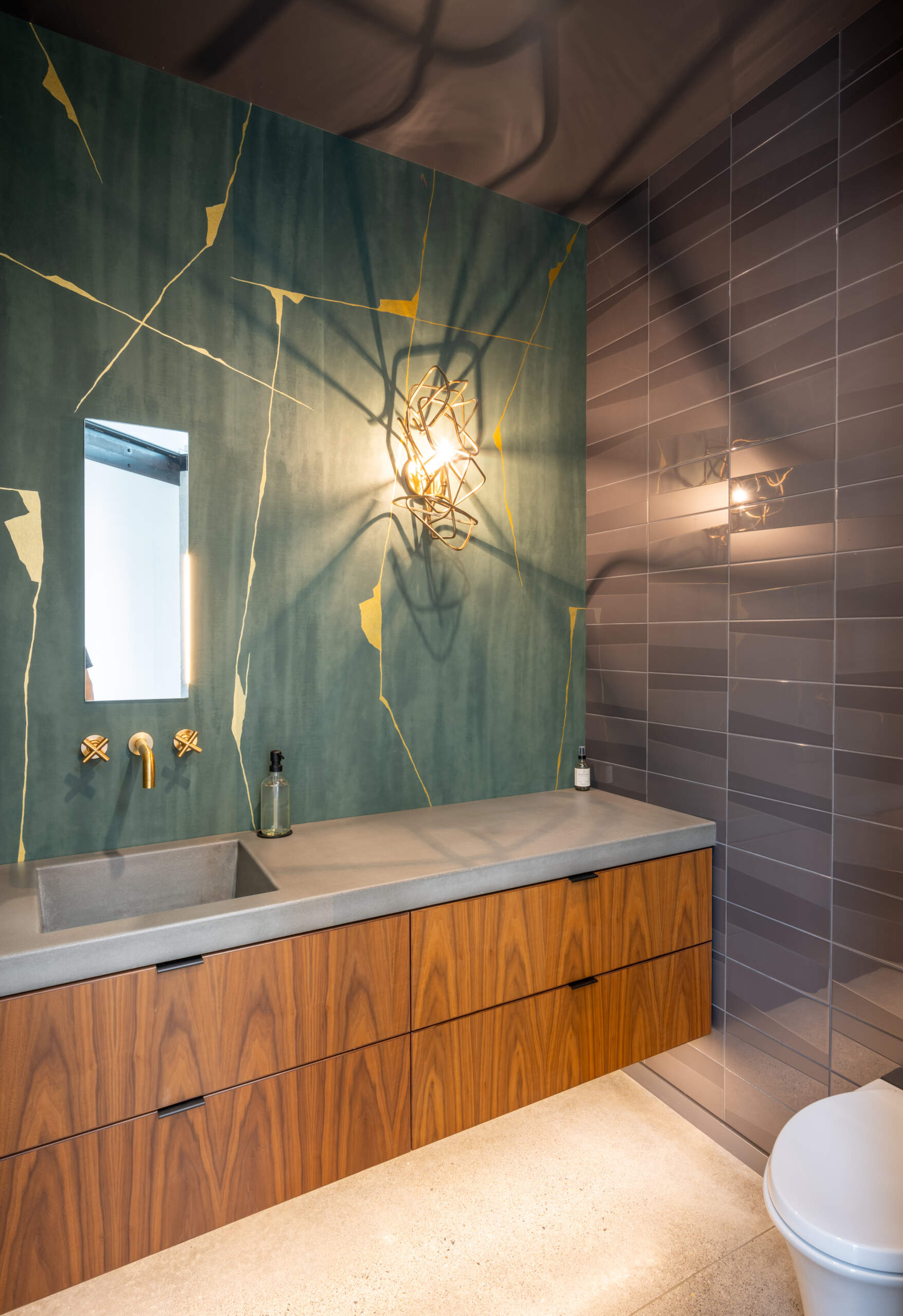 The guest bathroom, with its gold accents, follows the same durable material approach used throughout the home, like the concrete floor and counter.