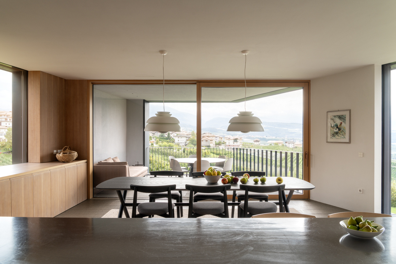 The dining space opens to a loggia overlooking the valley, blending interior comfort with expansive orchard views.