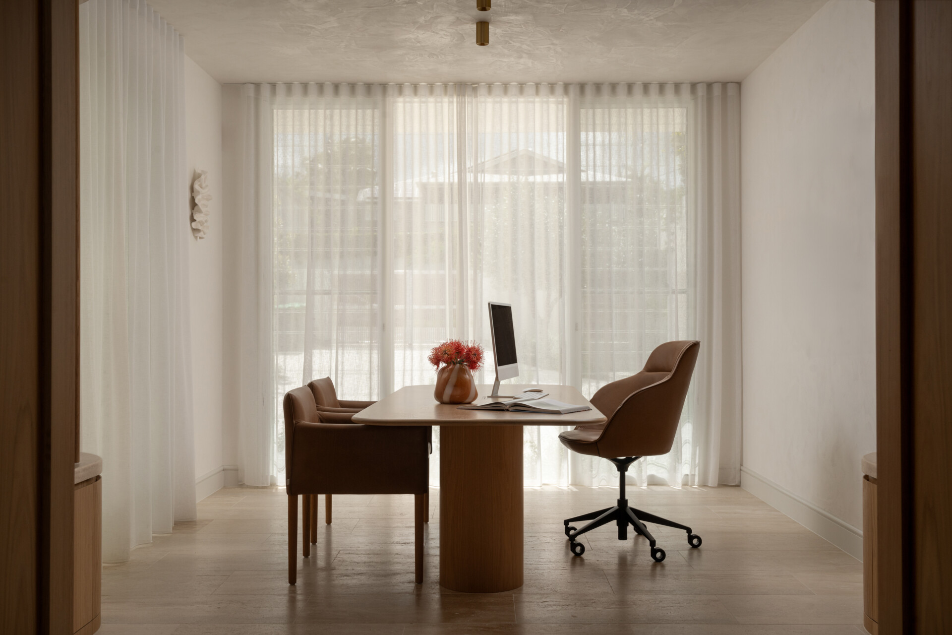 A sophisticated home office with custom oak doors, curved shelving, a travertine threshold, and soft Venetian-plaster light.