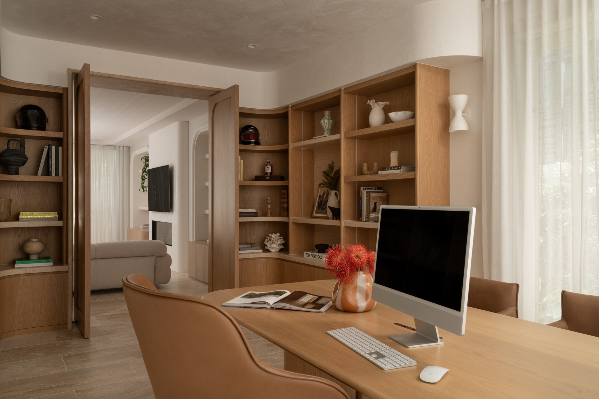 A sophisticated home office with custom oak doors, curved shelving, a travertine threshold, and soft Venetian-plaster light.