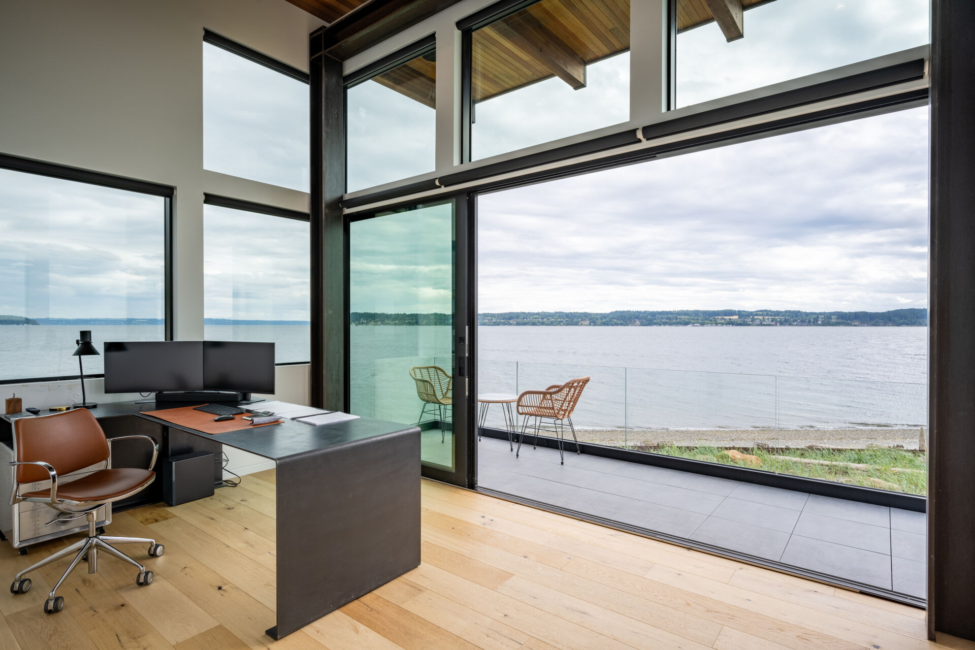 A modern home office opens to a balcony with glass railing, providing uninterrupted views.
