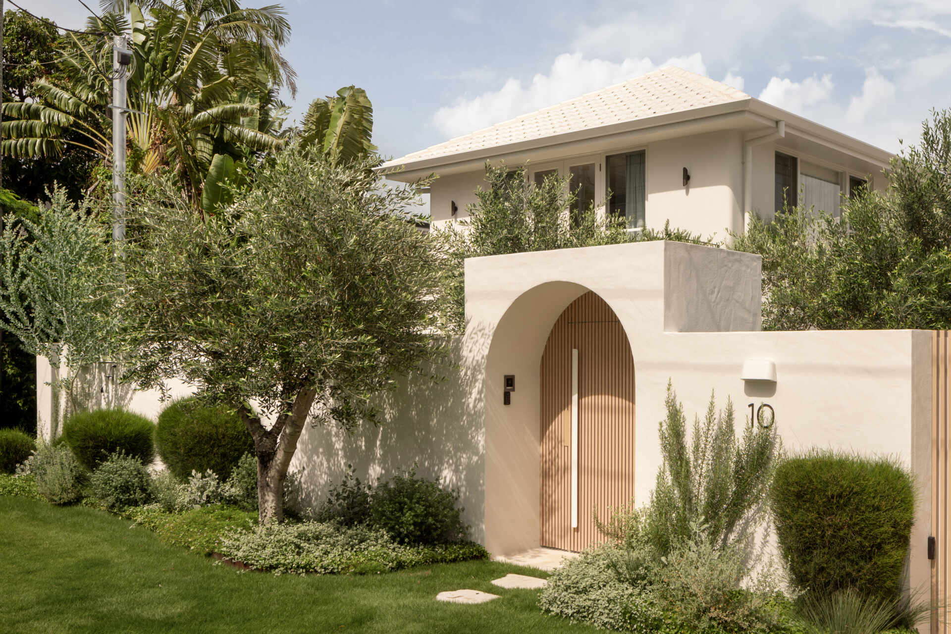 A Mediterranean-leaning entry framed by rocky textures and layered greenery, setting a soft and welcoming tone.