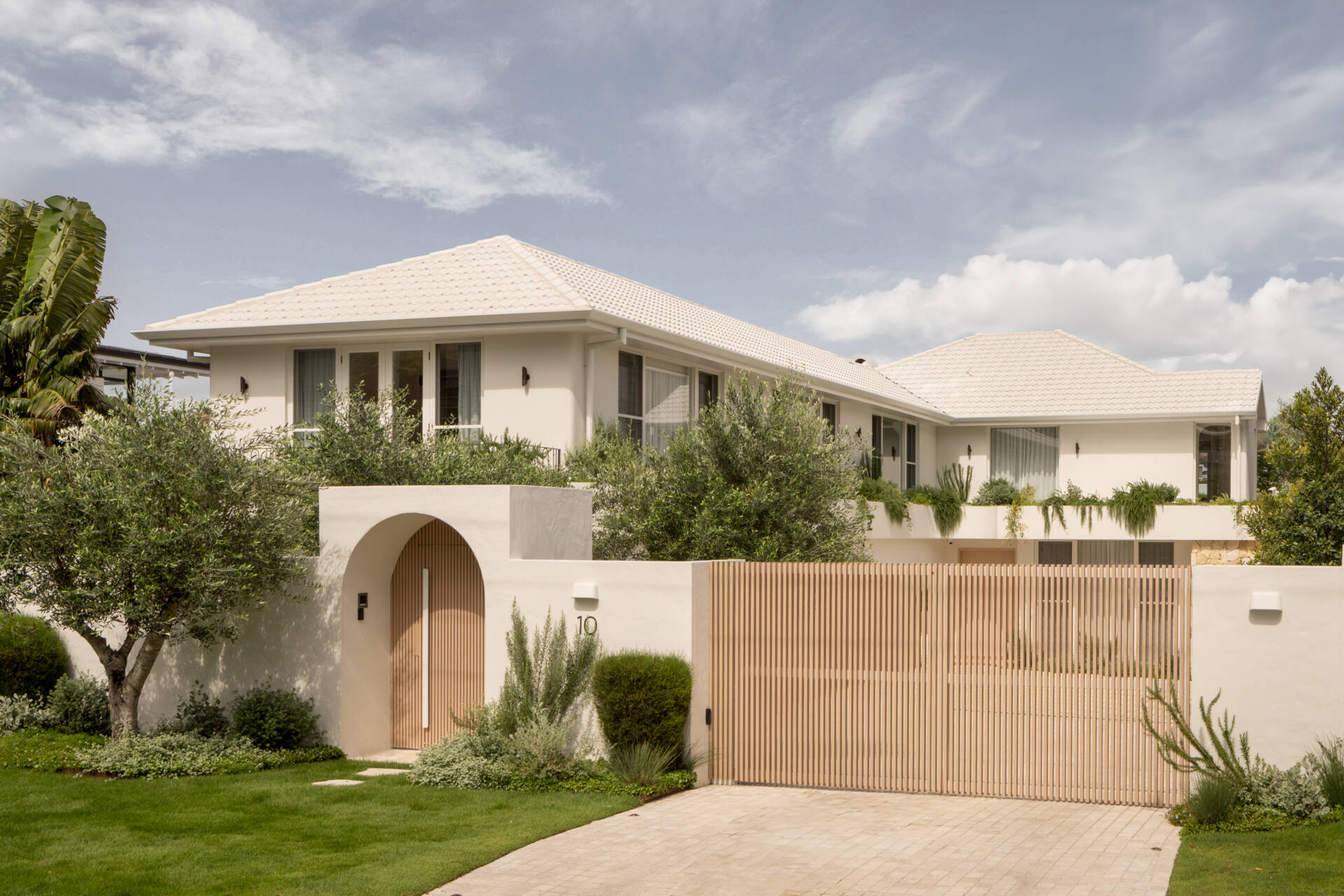 A Mediterranean-leaning entry framed by rocky textures and layered greenery, setting a soft and welcoming tone.