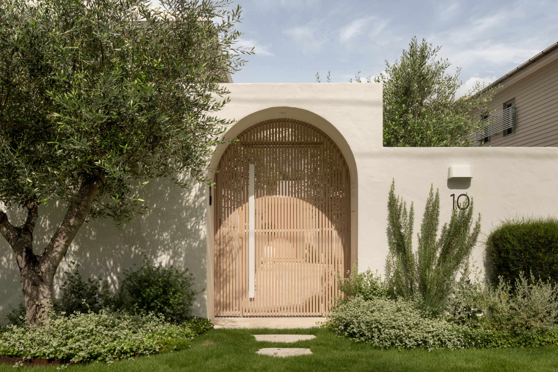A Mediterranean-leaning entry framed by rocky textures and layered greenery, setting a soft and welcoming tone.