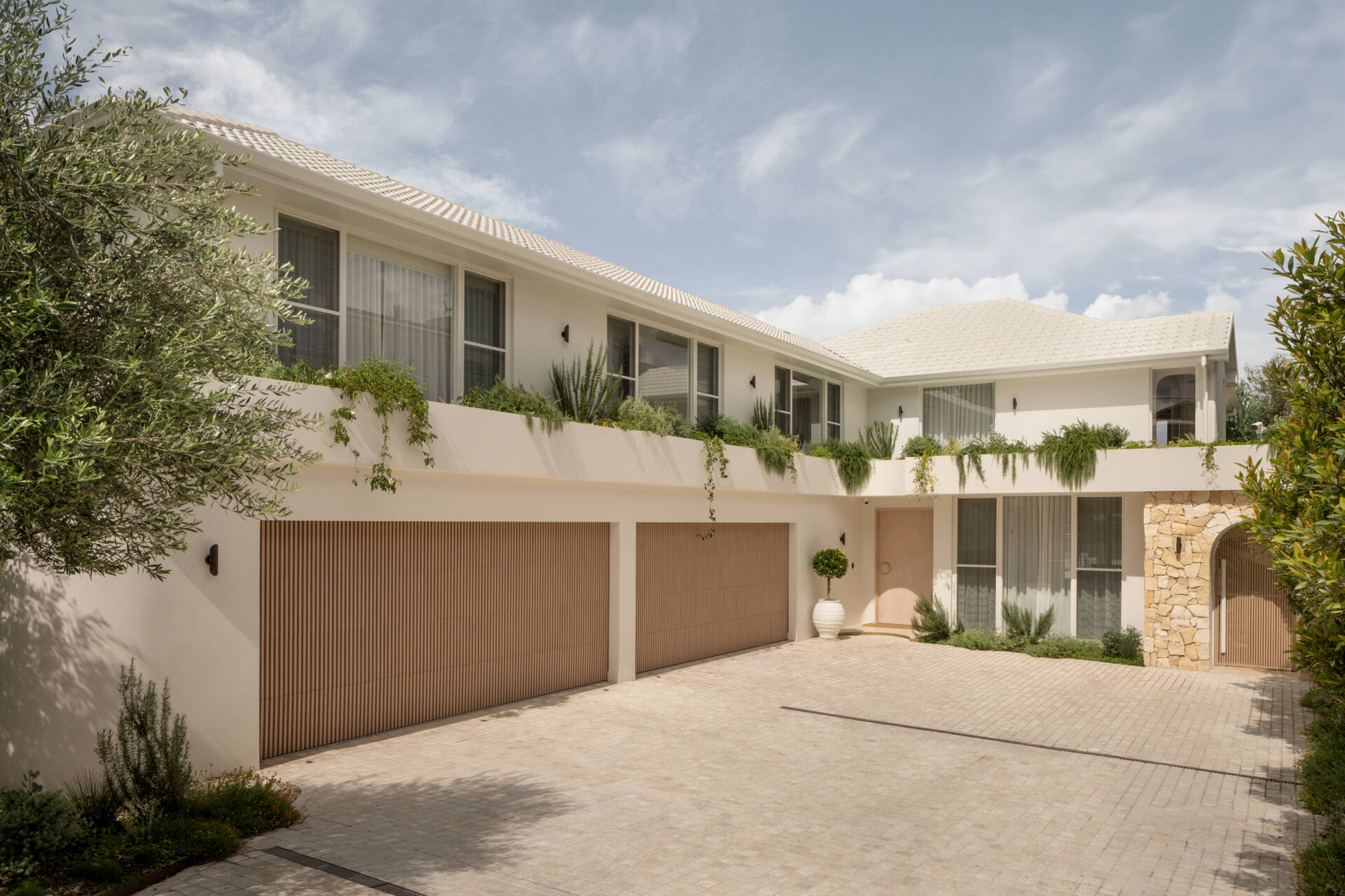 A Mediterranean-leaning entry framed by rocky textures and layered greenery, setting a soft and welcoming tone.