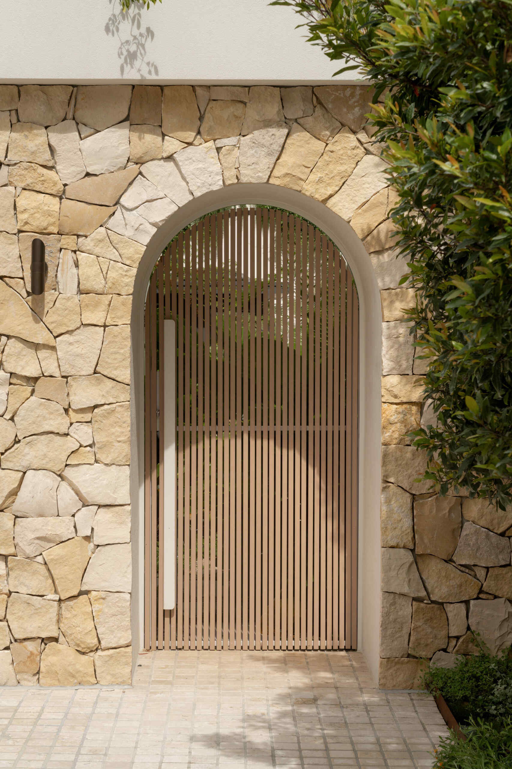 A Mediterranean-leaning entry framed by rocky textures and layered greenery, setting a soft and welcoming tone.