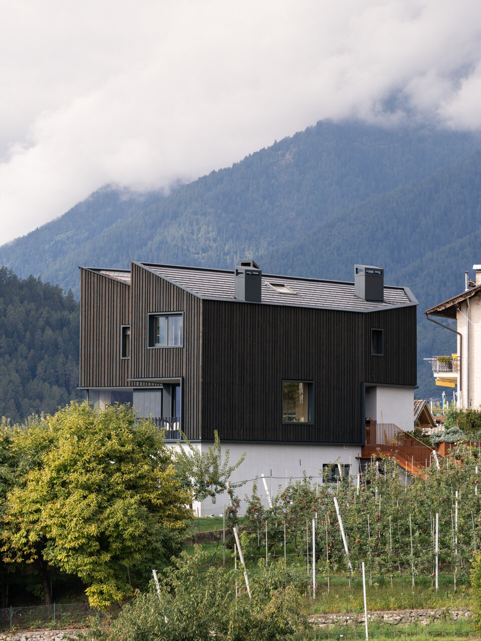 Black larch wood cladding gives this Italian hillside home a striking presence among apple orchards while staying rooted in local tradition.