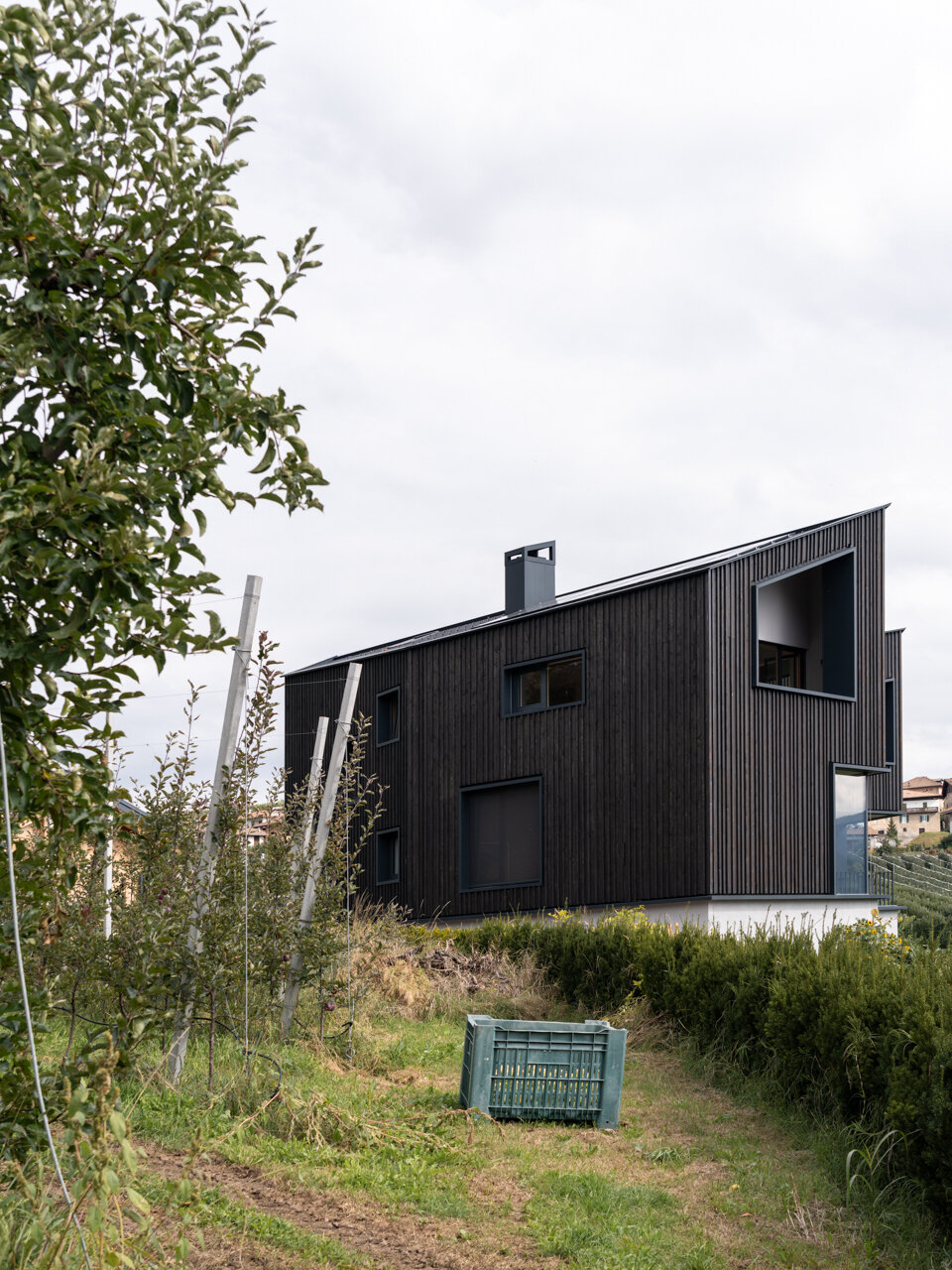 Black larch wood cladding gives this Italian hillside home a striking presence among apple orchards while staying rooted in local tradition.