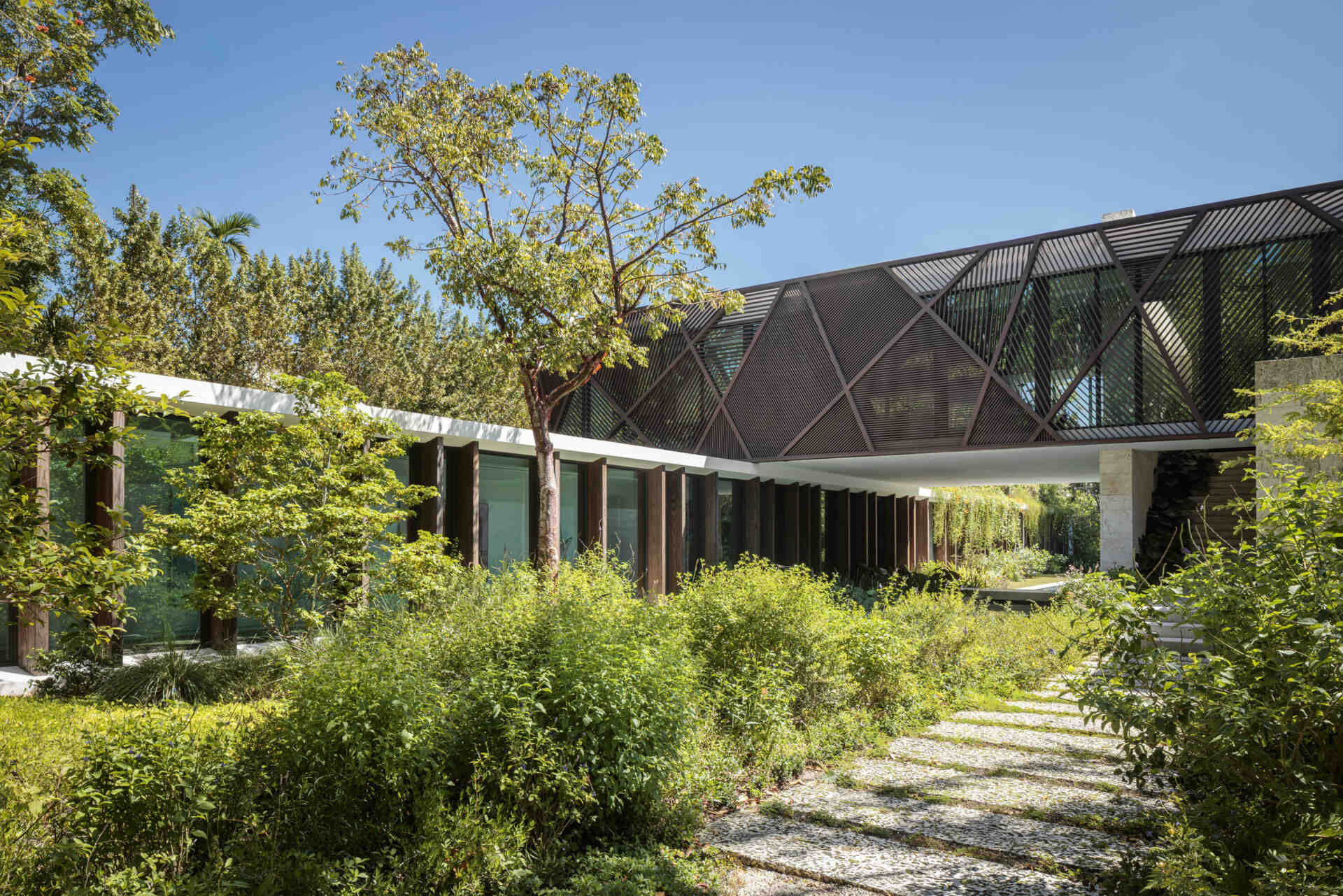 Two interlocking volumes define this Coconut Grove home, with wood panels and louvers creating warmth, shade, and a subtle connection to the surrounding greenery.