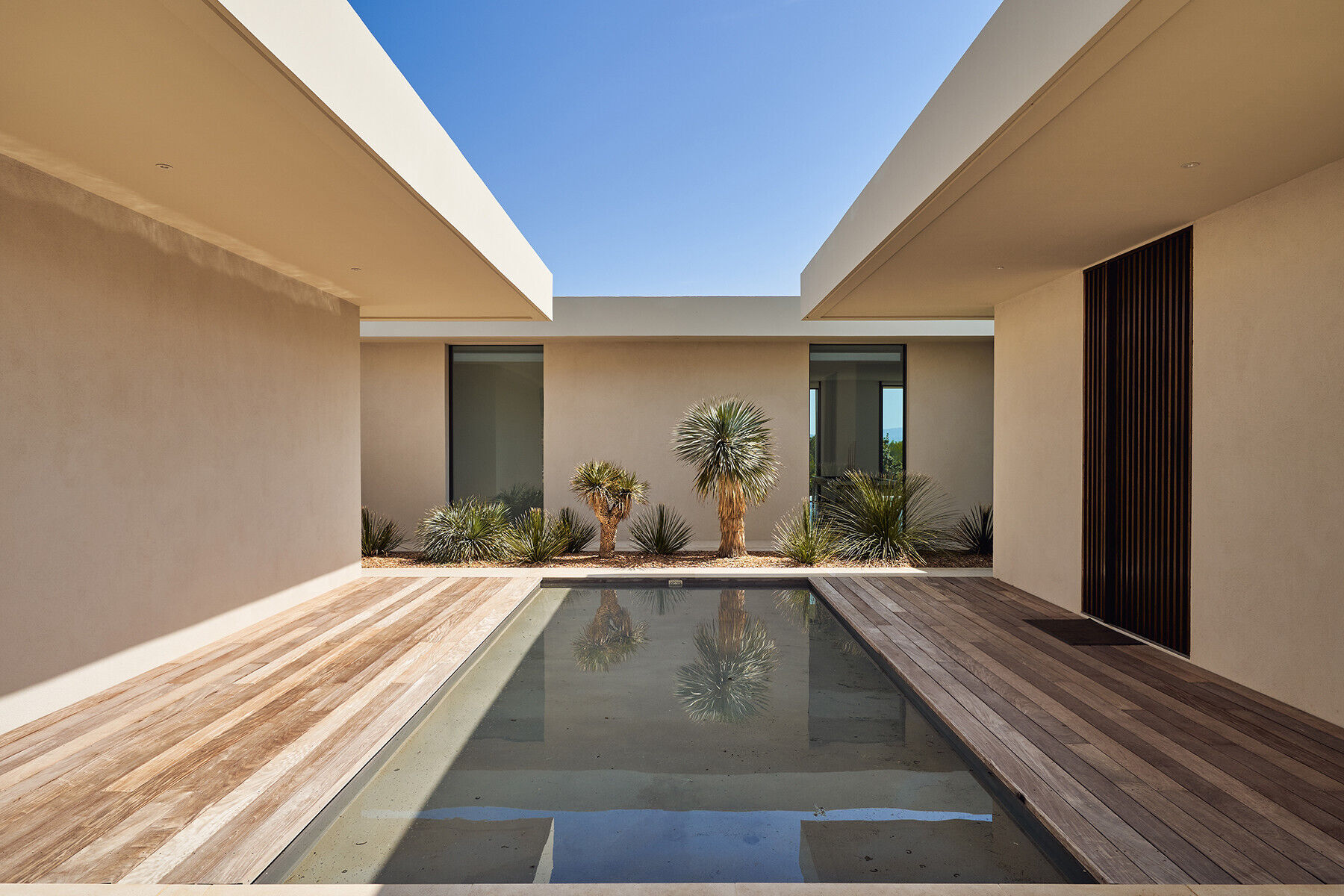 A reflective water feature and linear garden strip soften the entrance and introduce nature as a central design element.