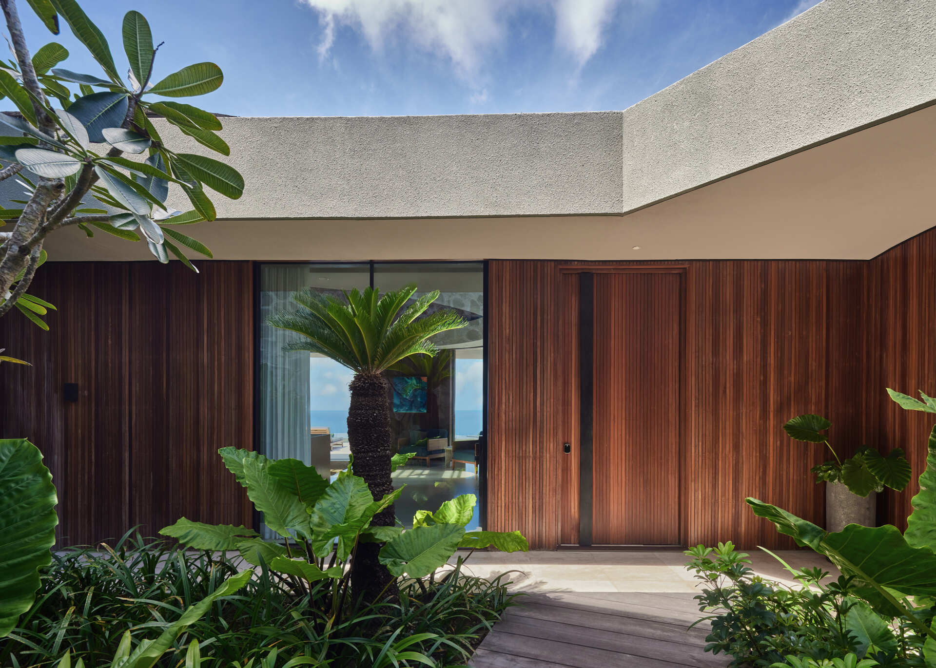 Warm teak, off white walls, and pale Palimanan stone create a calm exterior palette that lets form and landscape lead.