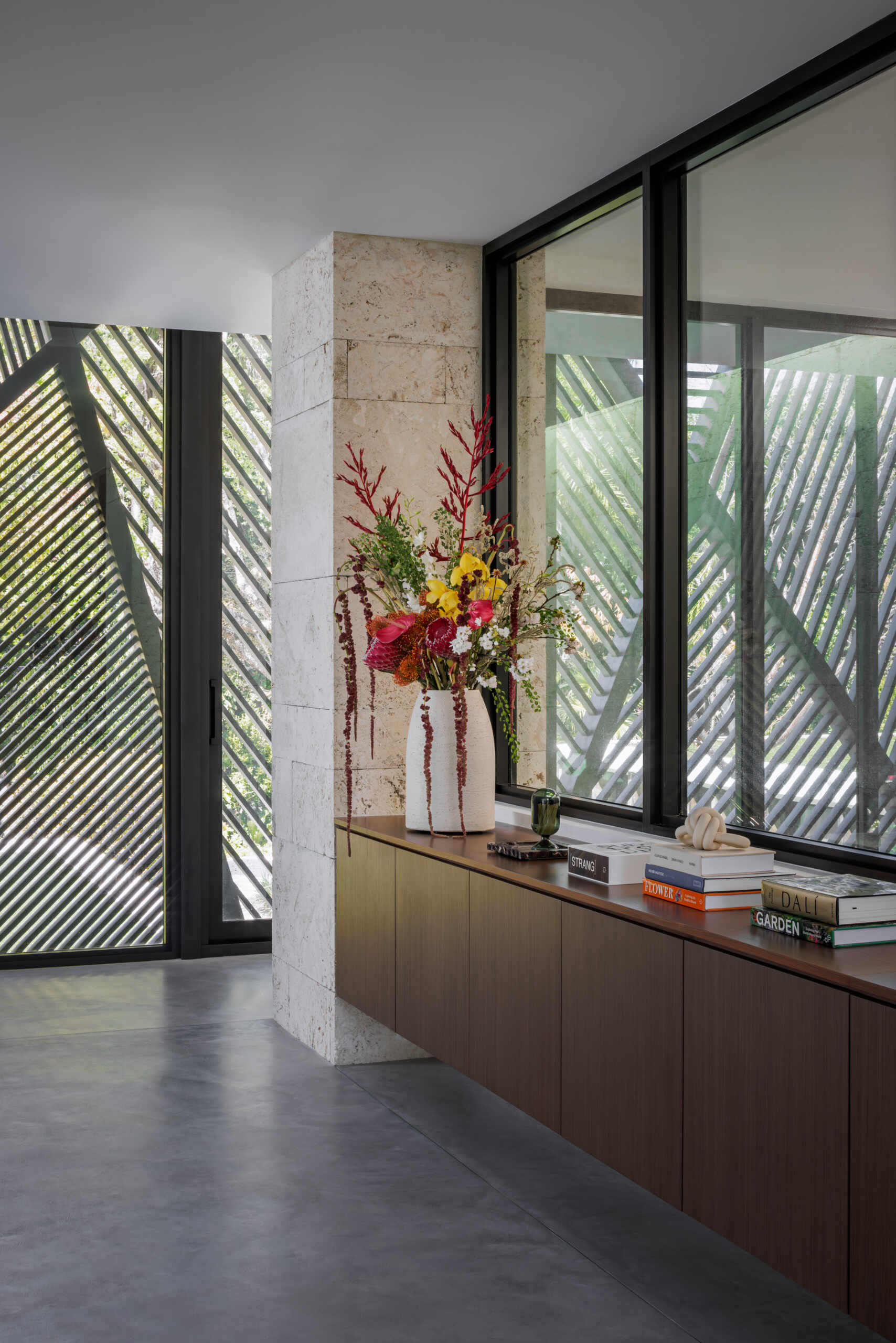 This living room feels light and composed, with creamy walls and a concrete floor that highlights the furniture’s forms. Curved sofas and plush chairs in soft caramel and cinnamon tones bring warmth, while layered rugs, wood elements, and sculptural side tables add subtle texture, and oversized artwork adds subtle color.