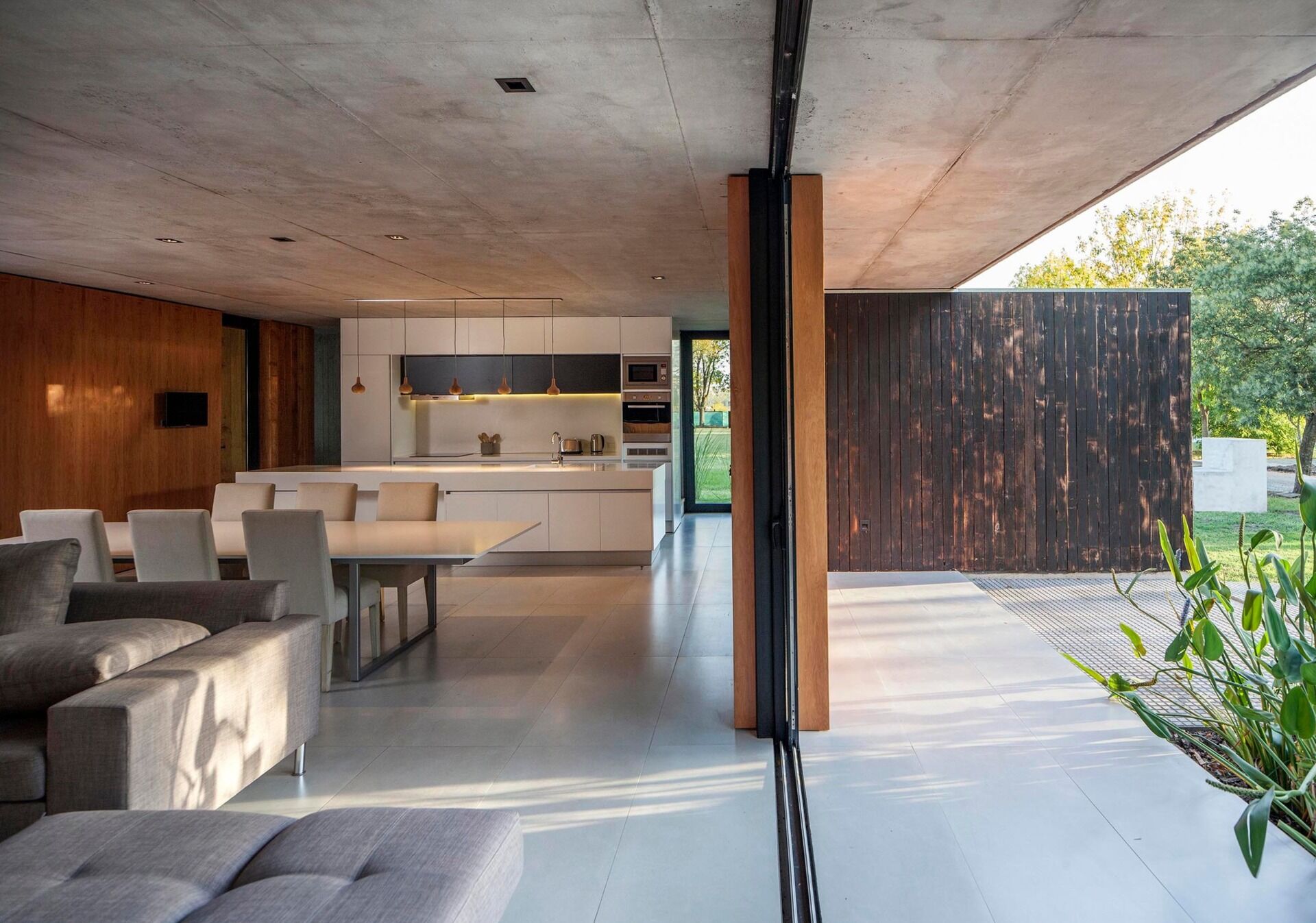 A minimalist white kitchen with a large island and wood pendant lights flows directly into the dining and living spaces.