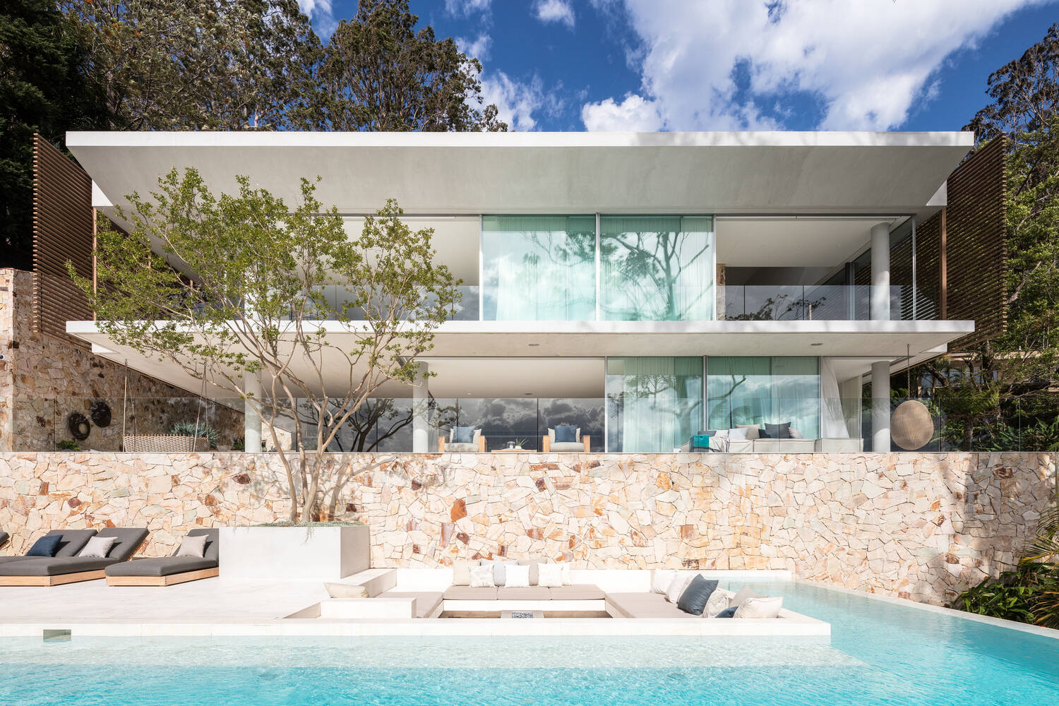Terraced concrete slabs and cascading levels are fully visible from the pool, highlighting the home’s floating design and connection to the slope.
