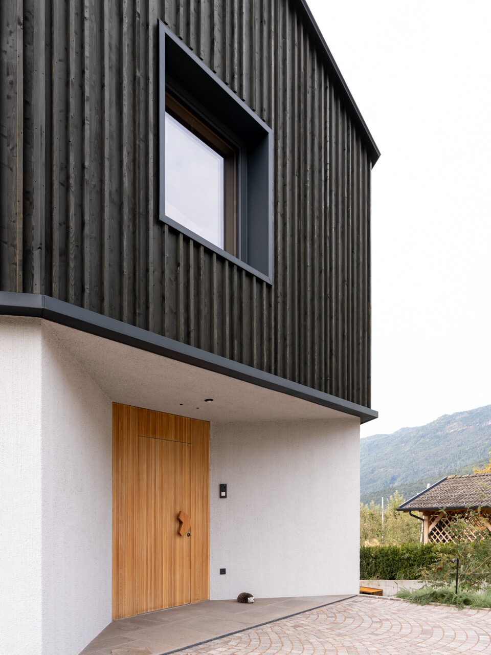 Porphyry stone paving and a custom larch door detail mark the transition from orchard landscape to contemporary interior.