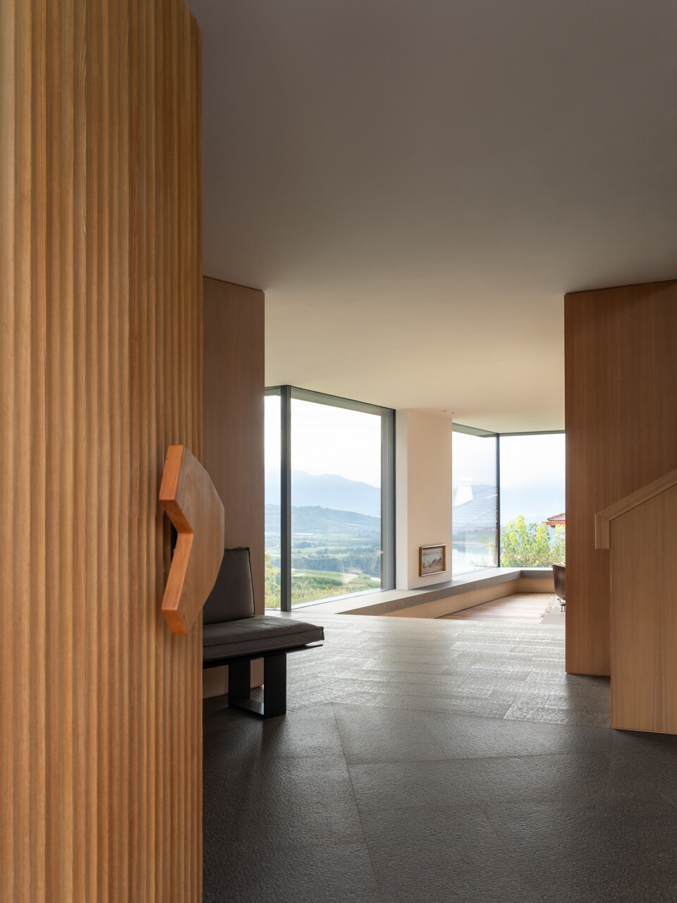 Porphyry stone paving and a custom larch door detail mark the transition from orchard landscape to contemporary interior.