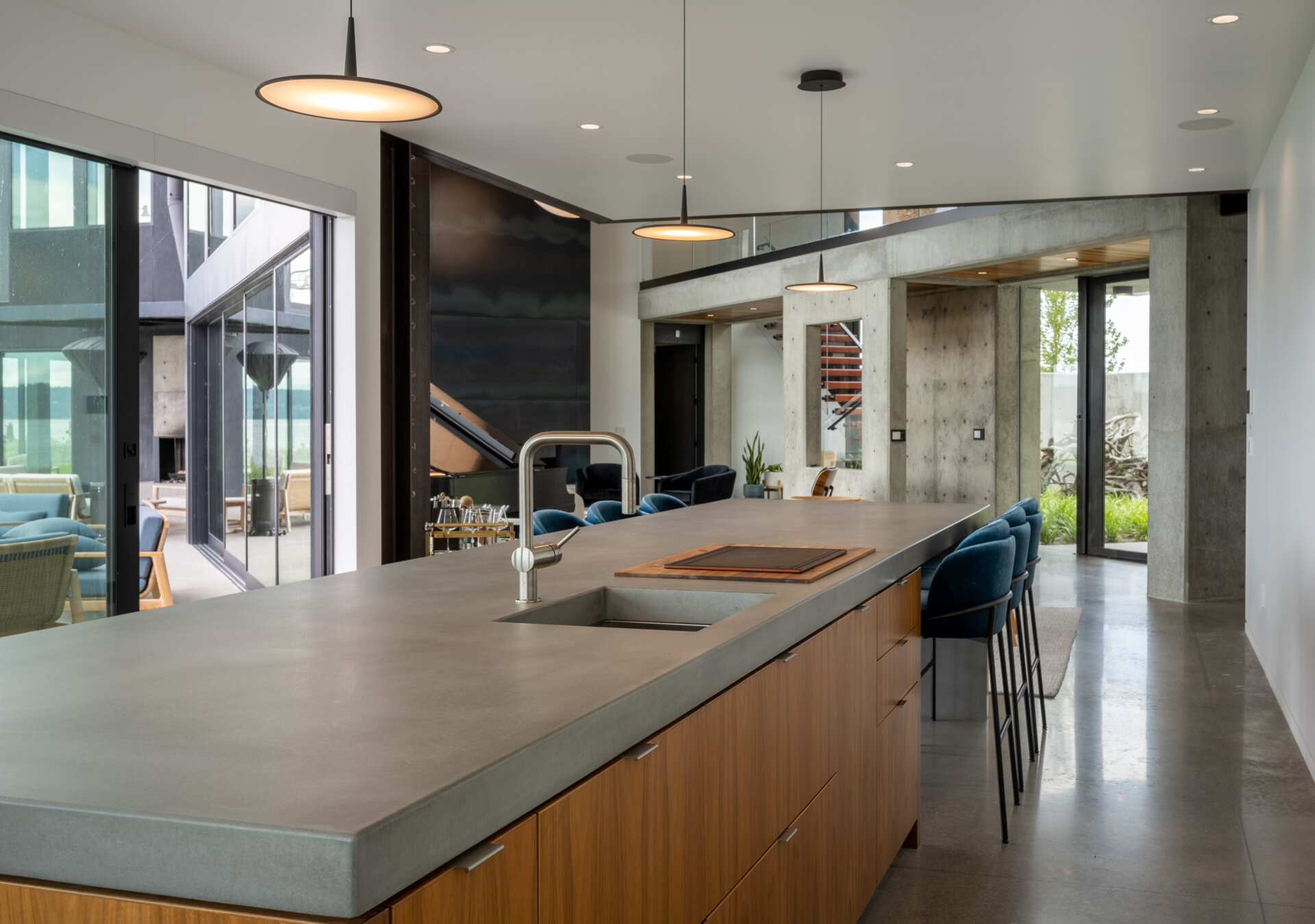 The kitchen has a long concrete island anchors the space, providing room for everyday use and casual gathering. Minimalist white cabinetry is paired with warm wood base units, keeping the palette restrained while adding subtle contrast. Floor to ceiling windows line the perimeter, drawing in natural light and uninterrupted water views. 