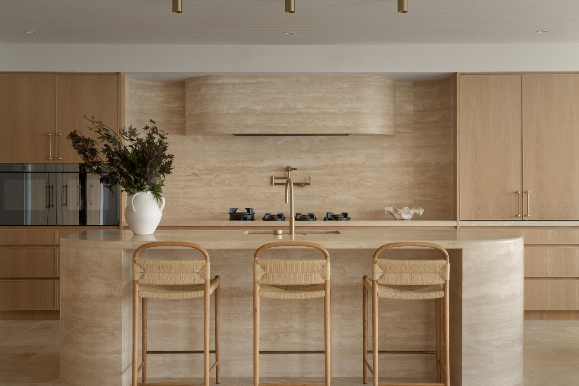 A travertine-rich kitchen with rounded, soft edges and a minimal Mediterranean palette. Nearby, a large walk-in pantry echoes the materials of the kitchen.