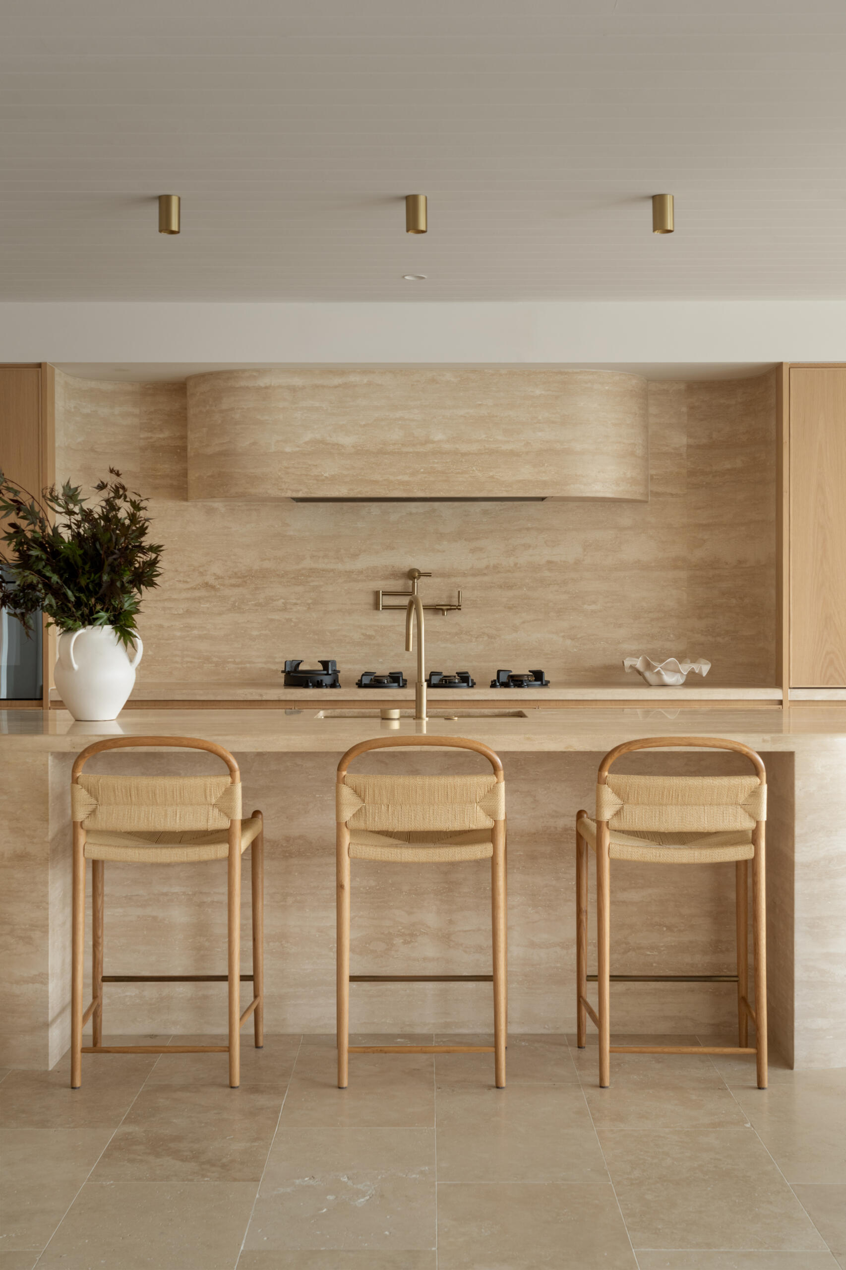 A travertine-rich kitchen with rounded, soft edges and a minimal Mediterranean palette. Nearby, a large walk-in pantry echoes the materials of the kitchen.