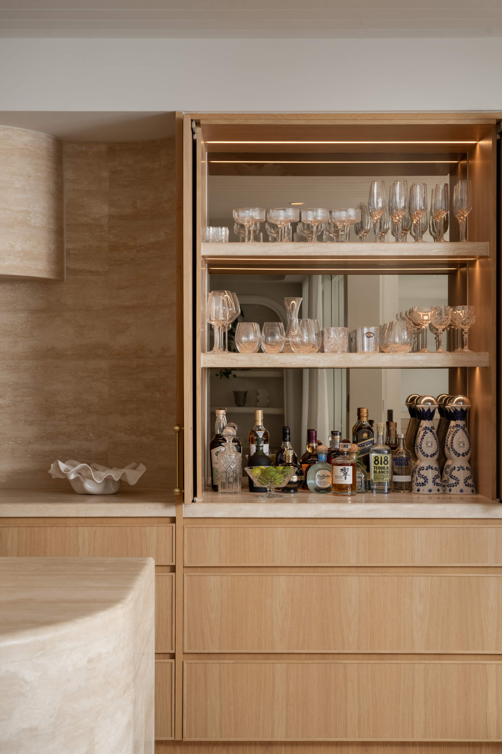 A travertine-rich kitchen with rounded, soft edges and a minimal Mediterranean palette. Nearby, a large walk-in pantry echoes the materials of the kitchen.