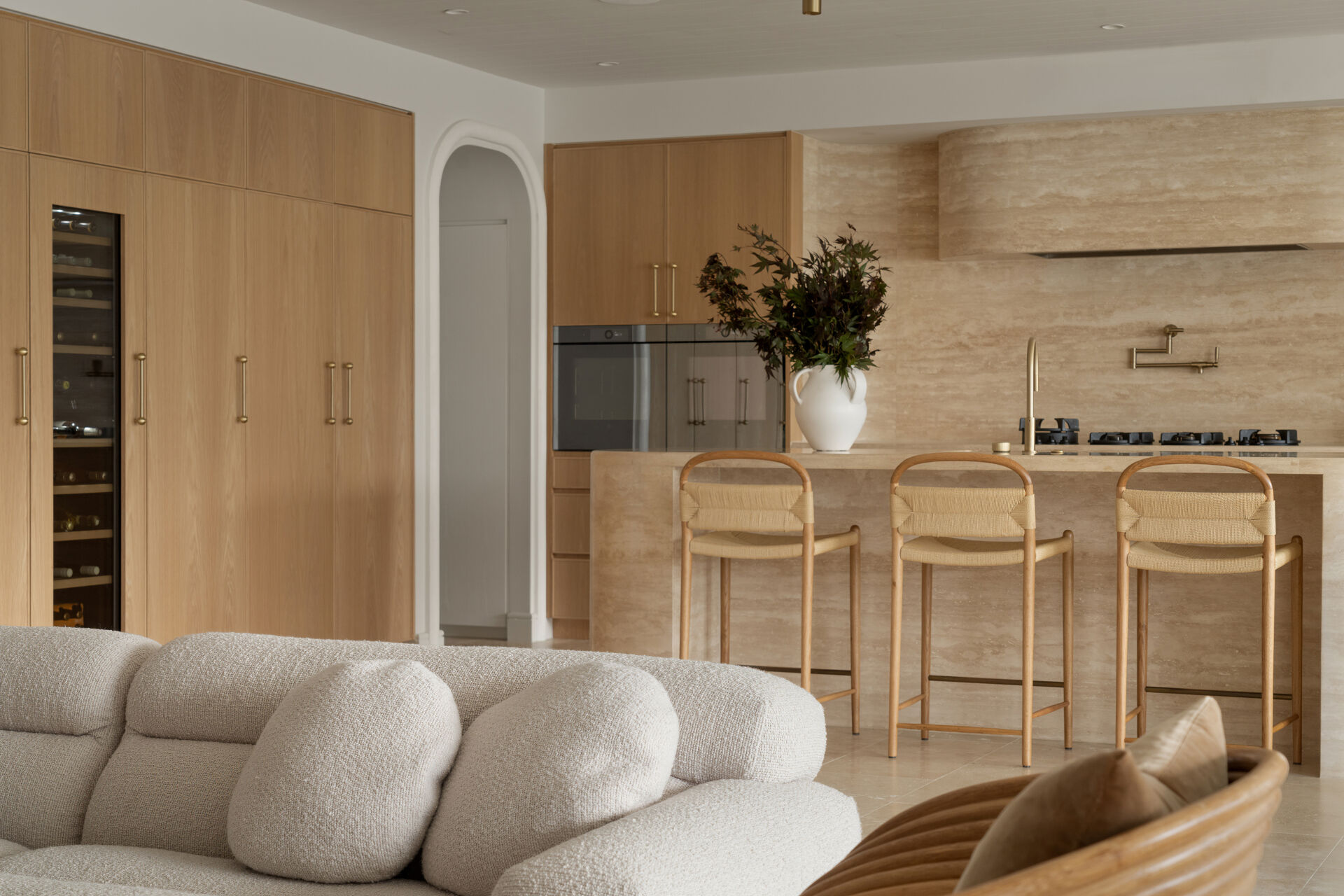 A travertine-rich kitchen with rounded, soft edges and a minimal Mediterranean palette. Nearby, a large walk-in pantry echoes the materials of the kitchen.