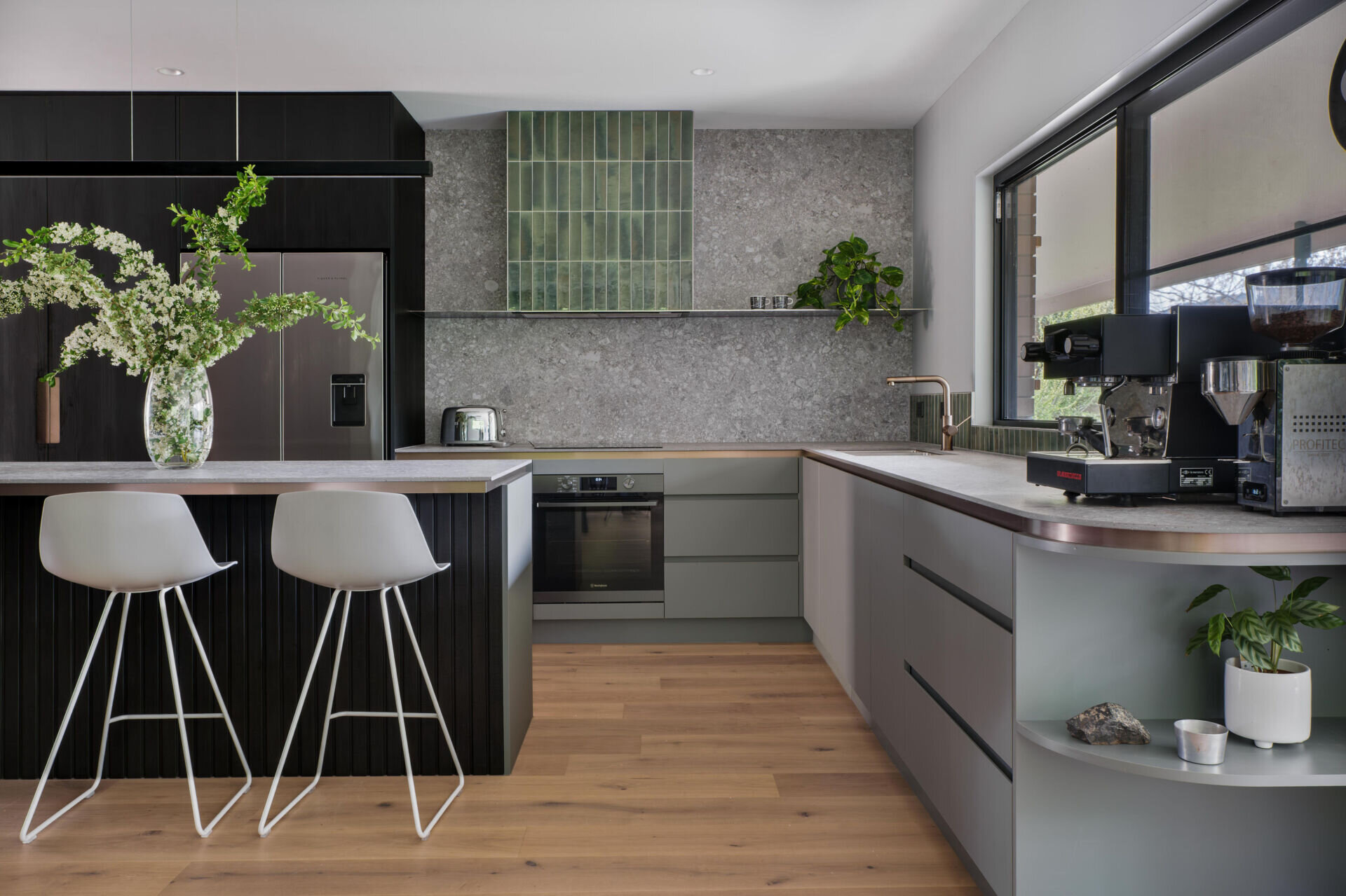A nature inspired kitchen with stone countertops, green joinery, a tiled hood and soft eastern light flooding through a new window.