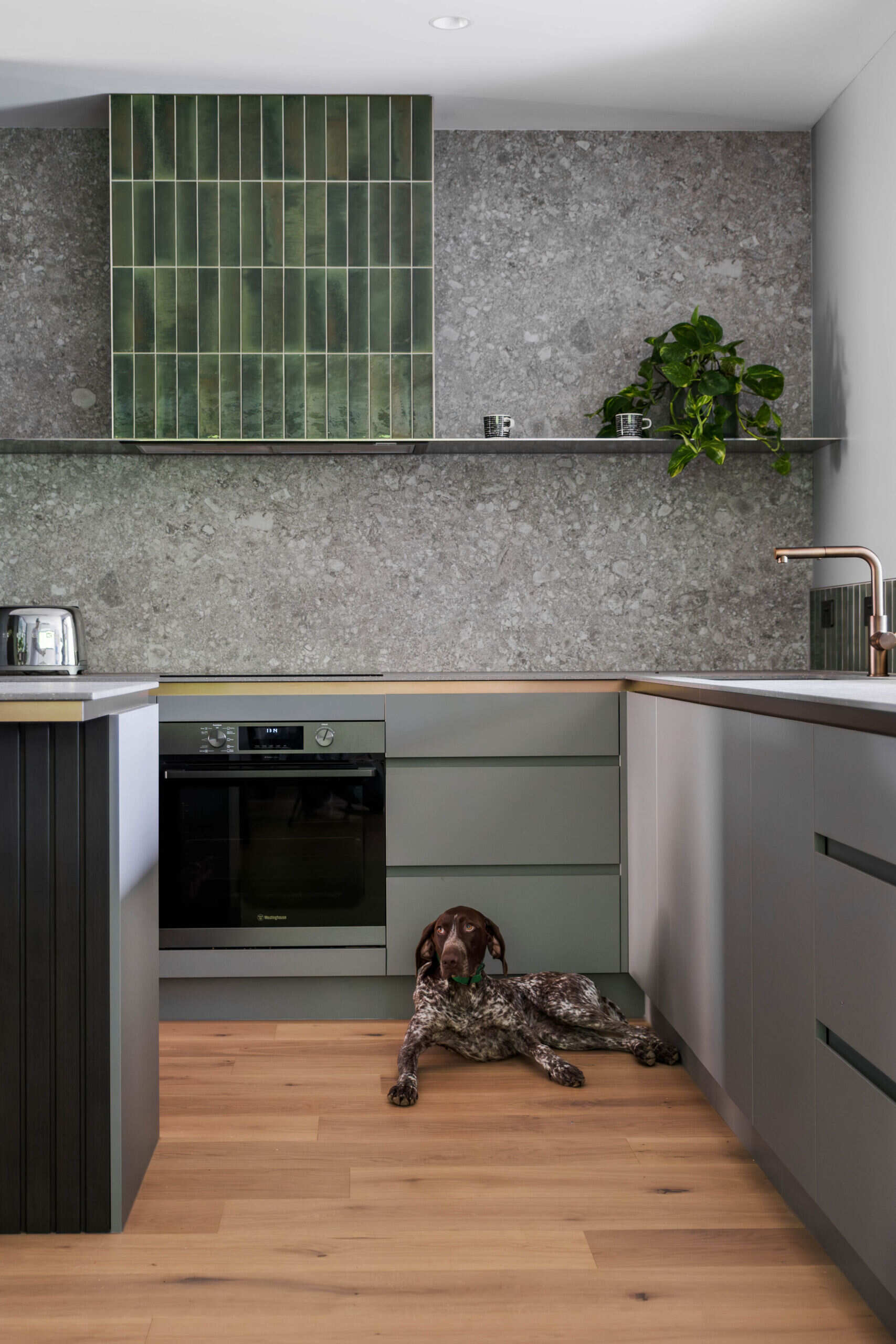 A nature inspired kitchen with stone countertops, green joinery, a tiled hood and soft eastern light flooding through a new window.