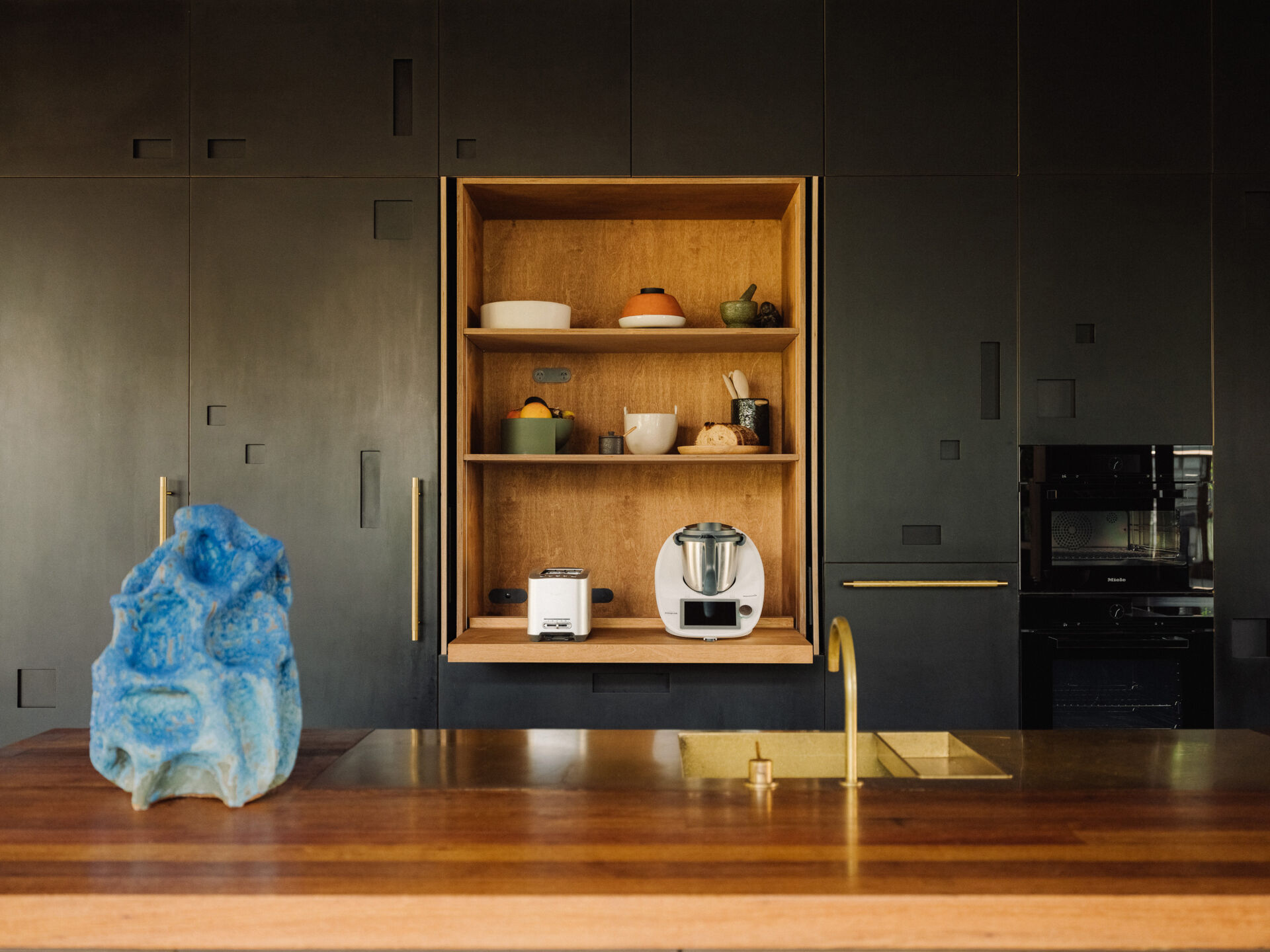 A 9.2 metre recycled hardwood island, which doubles as the dining table, stretches through to the kitchen. A full wall of cabinetry made from Paperock creates small niches that mimic dappled forest light, and offers generous storage without visual clutter. 