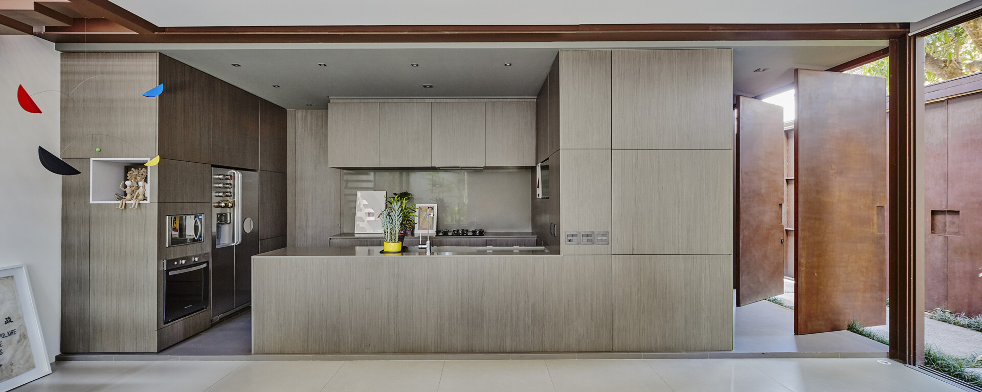 Rather than separating entry from everyday living, the house opens directly into its social areas. The kitchen sits prominently within this space, designed with minimalist, hardware free cabinetry that keeps the room visually calm.